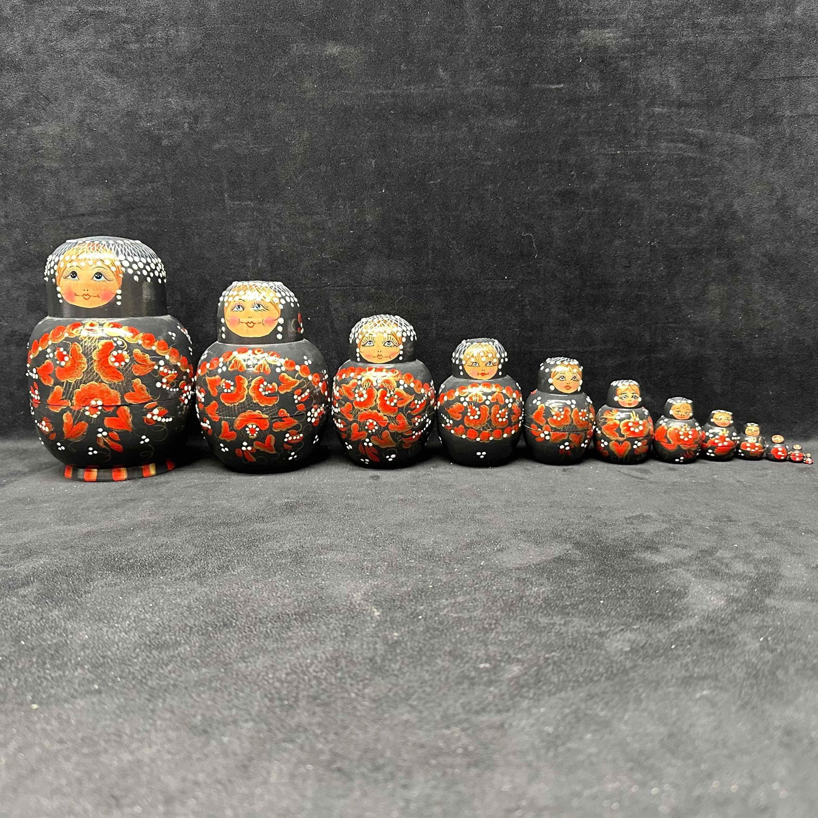 Large Set of 12 Hand Painted Russian Nesting Dolls Black with Red Gold Floral Design: Hand-painted Russian nesting dolls featuring a striking black background with red, gold, and white floral accents. This complete set includes twelve dolls, each fitting inside the next, with the large