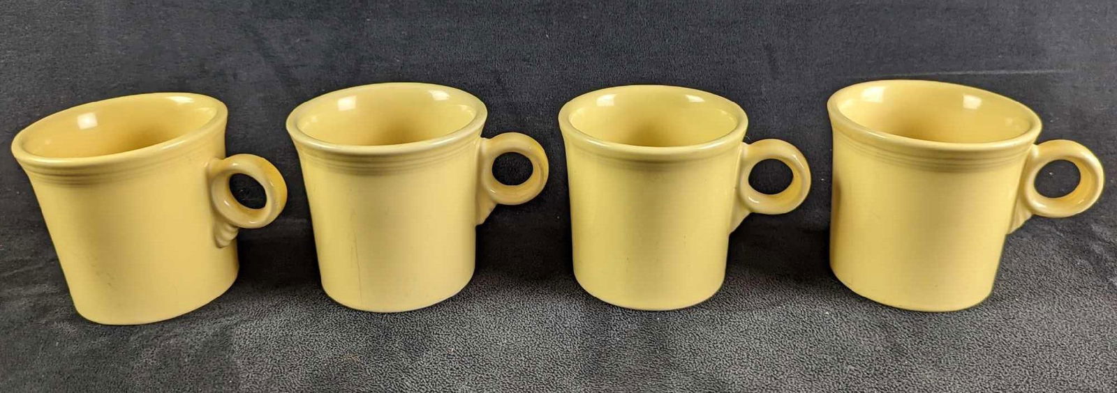 4 Yellow Sunflower HLC Fiesta Mugs: 4 Yellow Sunflower HLC Fiesta Mugs. Each is approx 5" x 2 1/2" x 3 1/2" and together they weigh 3.84lbs. The mugs are in good,used condition with some signs of wear and scratches inside the mugs and o