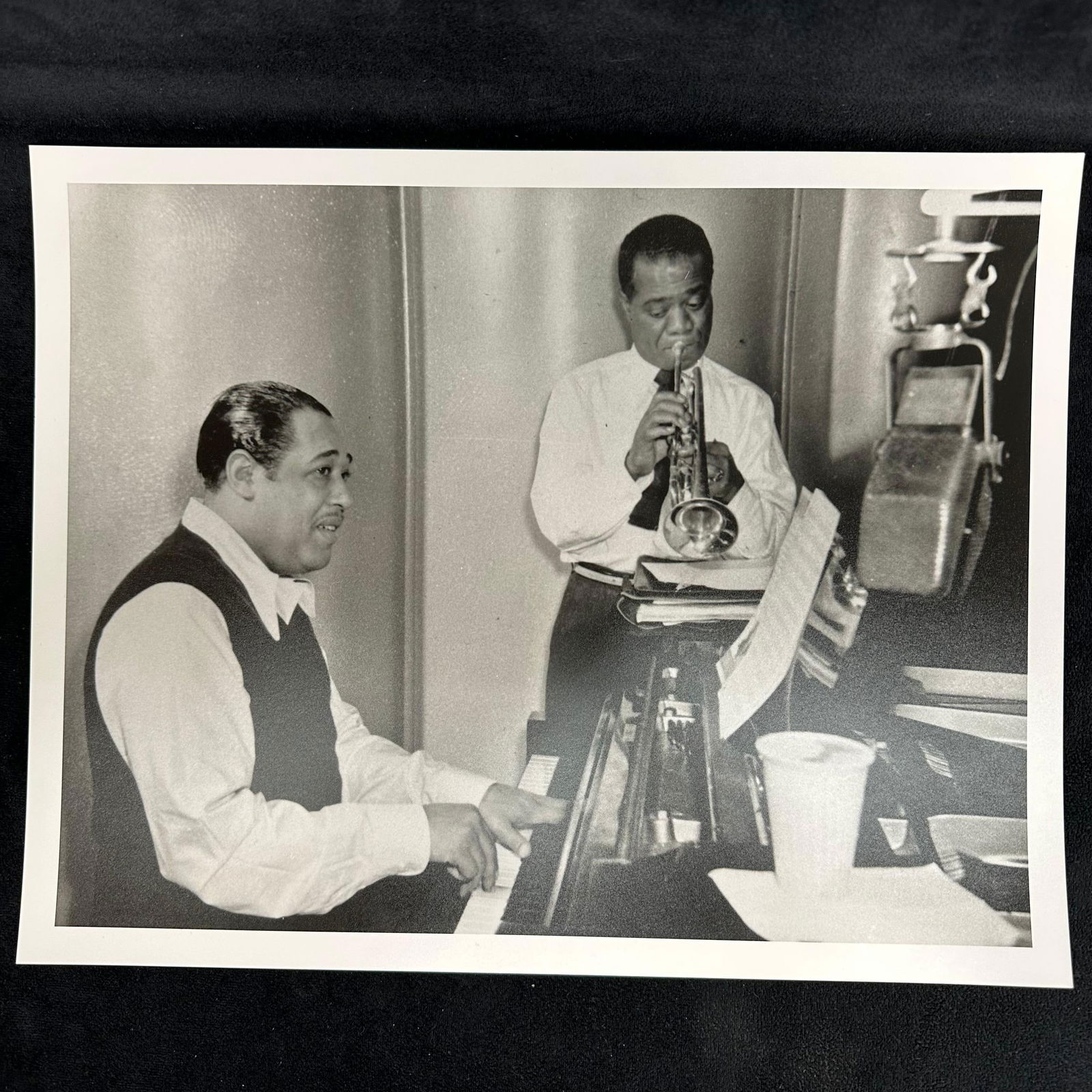 Duke Ellington and Louis Armstrong in Studio Black and White Analog Photograph Print: Black and white photograph featuring two jazz legends in a recording studio: Duke Ellington at the piano and Louis Armstrong playing trumpet. The image captures an intimate moment of collaboration bet