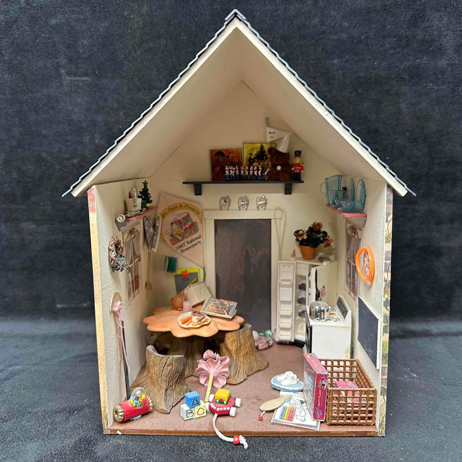 1996 Miniature Dollhouse Room Box Garden of Delights: Handcrafted miniature room box with painted cottage exterior and fully furnished interior including table, chairs, kitchenware, toys, and decor. Marked on the back with 1996 NAME National “Garden of