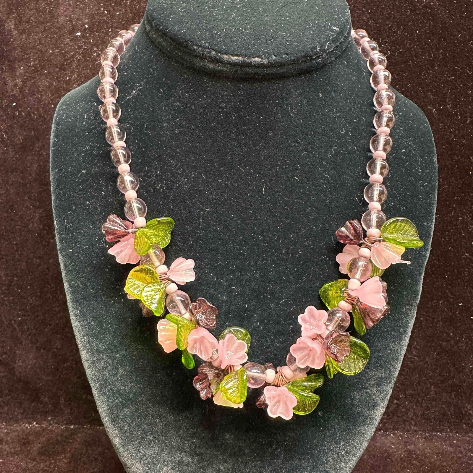 Murano Lamp Work Art Glass Purple Flower Bead Floral Beaded Necklace G16: Necklace with purple colored glass flower shaped beads with beautiful designs on each. The necklace features floral and green colored accents. The necklace features a barrel clasp closure. This item i