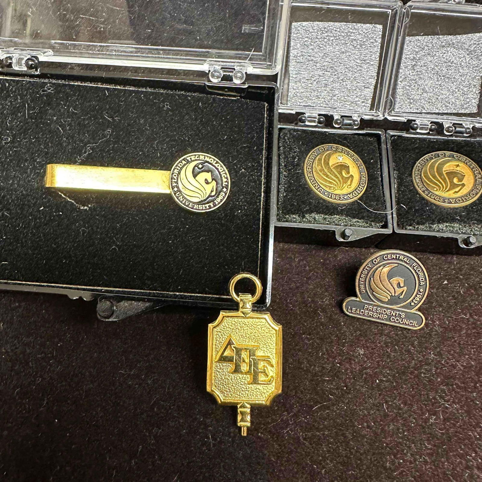 UCF Pins and Tie Clip Gold-Filled Lapel Pins: Group includes University of Central Florida tie clip, UCF lapel pins, President’s Leadership Council pin, fraternity pendant, and a pair of 1/10 10KT gold-filled pins. Light wear consistent with ag