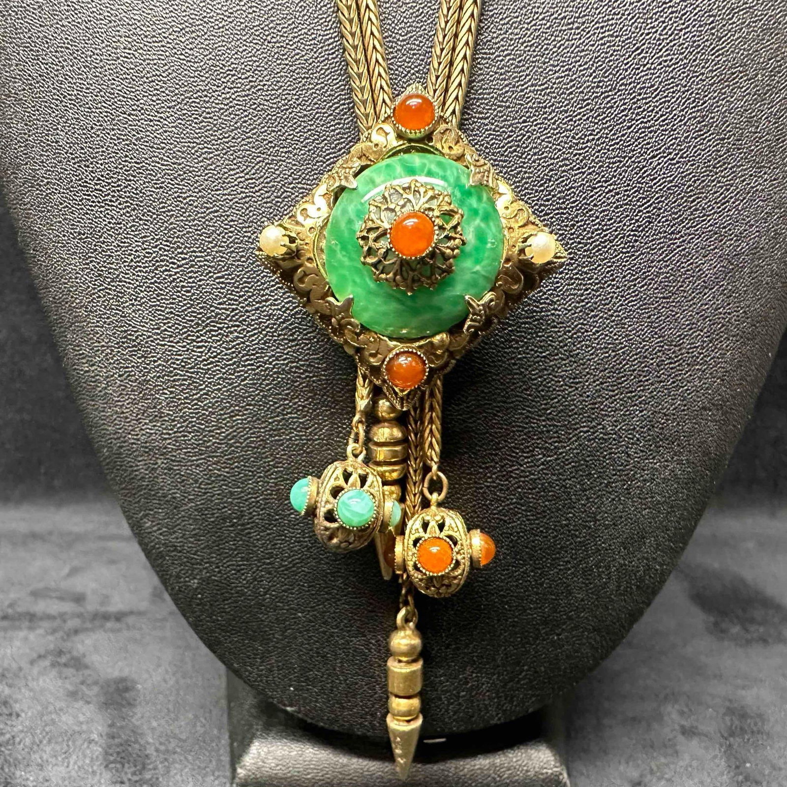 Lariat Bolo Necklace Bohemian Tribal Revival Style Statement Faux Stone Dangle and Centerpiece: This gold tone lariat bolo necklace features faux stone and pearl accents on the centerpiece and dangle pieces. Doubles strand with slide centerpiece. This item is in good pre-owned, previously displa