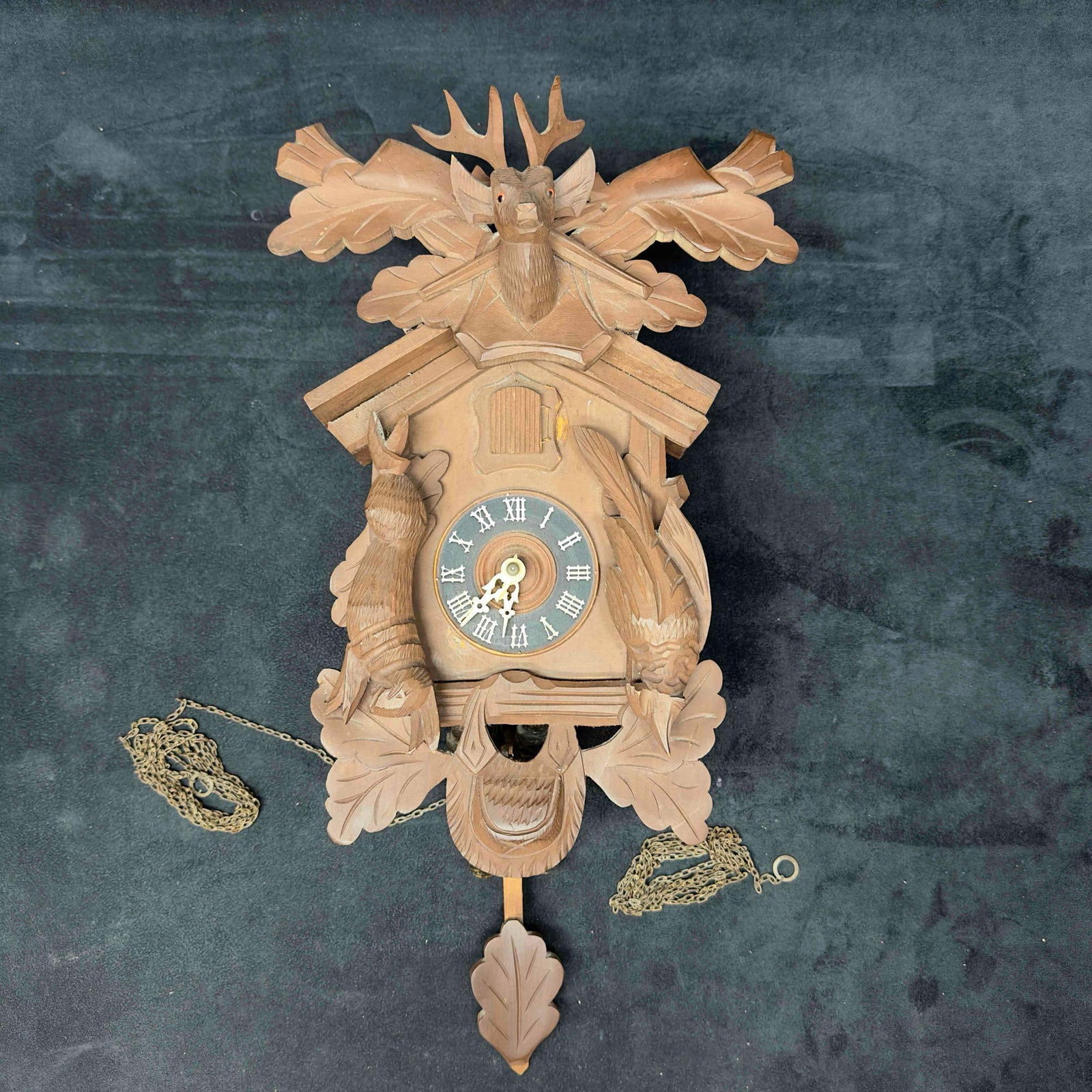 Wall Cuckoo Clock Deer Birds Forest Hunter Themed Brass Pinecones Made in West Germany: Wall Cuckoo Clock Deer Birds Forest Hunter Themed Made in West Germany. This hand carved clock features birds and a deer with antlers and rifles at the top. Two brass pine cones hang from the bottom w
