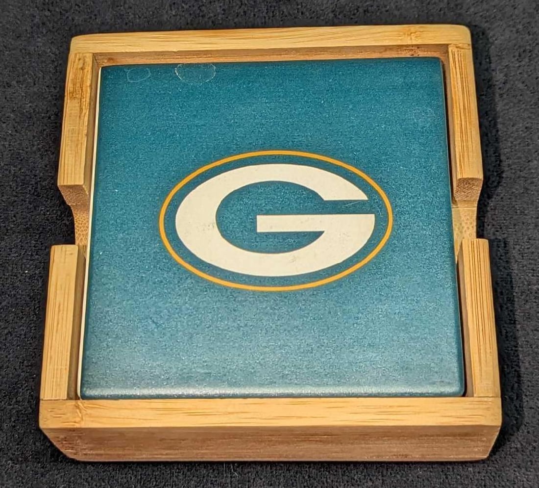 4 Ceramic Green Bay Packers Football Coasters: 4 Ceramic Green Bay Packers Football Coasters. Each coaster is approx 3 7/8" x1/4" x 3 7/8". The four coasters and wooden stand are approx 4 1/2" x 4 1/2" x 1 3/4" and it weighs 1.14lb. There are some