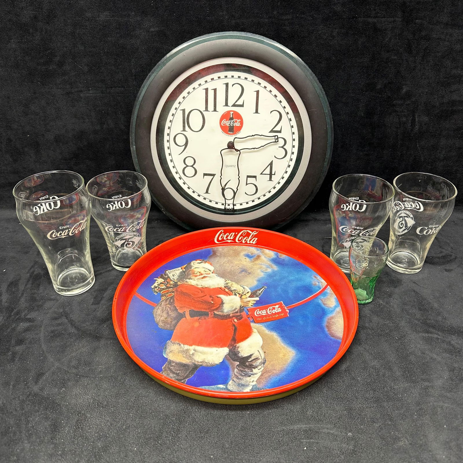 Coca Cola Collectible Lot Clock Santa Tray Glassware Set: Coca-Cola collector’s lot featuring a vintage-style Coca-Cola wall clock, a Santa “Around the World” metal tray, and a set of five Coke glasses. The glasses include four classic “Enjoy Coc