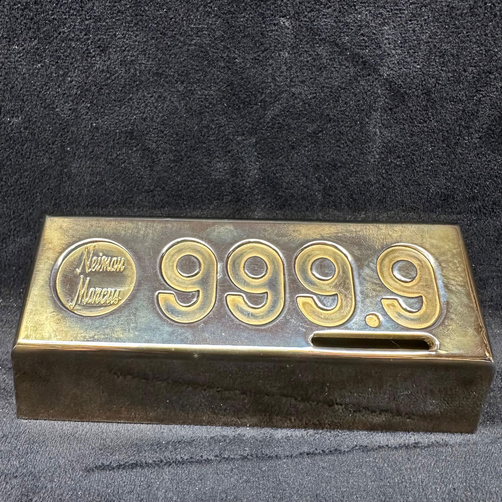 Neiman Marcus Brass Gold Bar Style Coin Bank 999.9 Paperweight: Neiman Marcus brass coin bank designed in the shape of a gold bar marked 999.9. Features an embossed Neiman Marcus logo and a bottom access panel. Heavy, solid construction with reflective finish. Sho