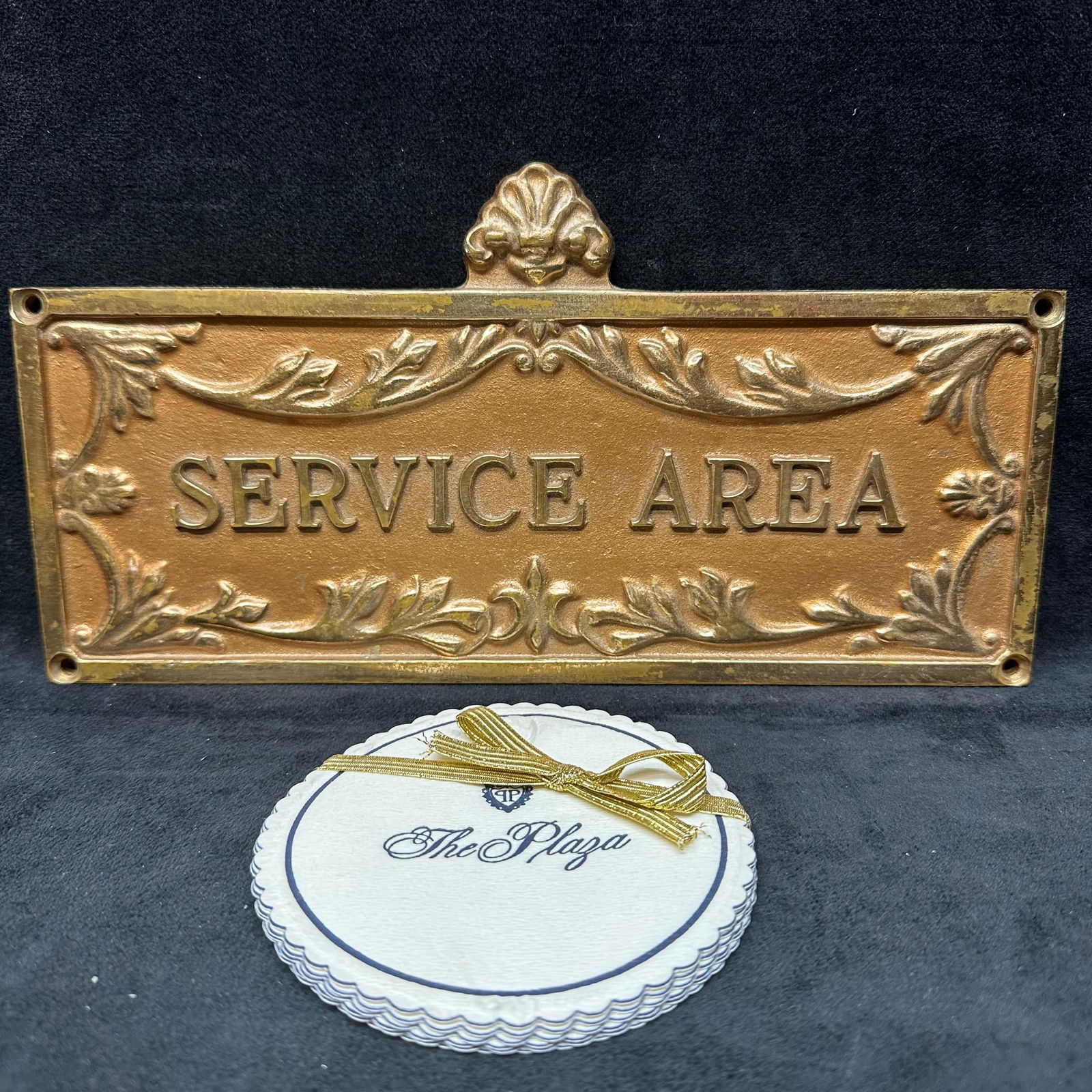 Plaza Hotel NYC Brass Service Area Sign and Plaza Hotel Coasters Lot New York: Vintage brass Service Area wall sign from The Plaza Hotel in New York City, featuring ornate raised scroll and leaf detailing with mounting holes on each corner. Includes a set of Plaza Hotel round sc