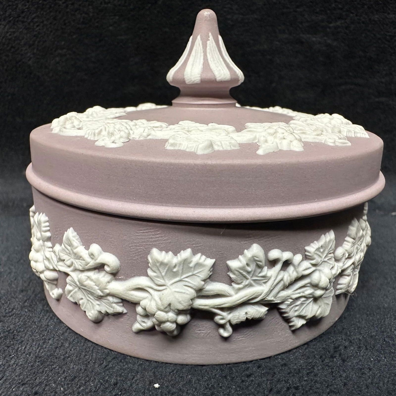 Bas Relief Lilac Purple Wedgwood Round Jewelry Trinket Box with Grapevine Lid: A purple lilac and white matte finish trinket box, Wedgwood, and their classic piece of pottery Jasperware range. Engraved on the bottom is Made in England, Wedgwood. The piece is purple lilac and whi