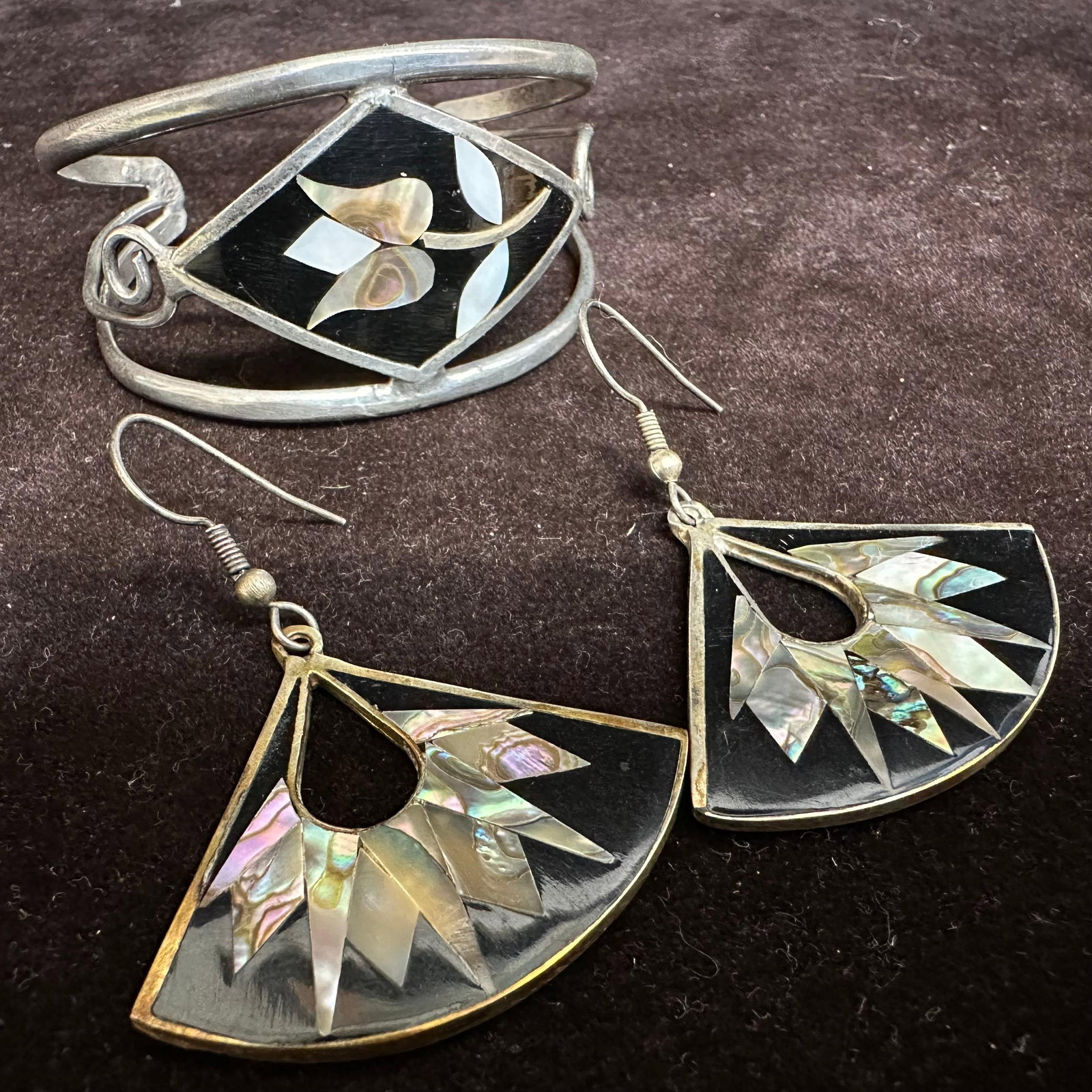 Alpaca Mexico Abalone and Mother of Pearl Inlay Bracelet and Earring Set O97: Vintage Alpaca Mexico jewelry set, including one cuff bracelet and one pair of fan-shaped dangle earrings. Features black resin panels inlaid with abalone and mother-of-pearl in floral and sunburst de