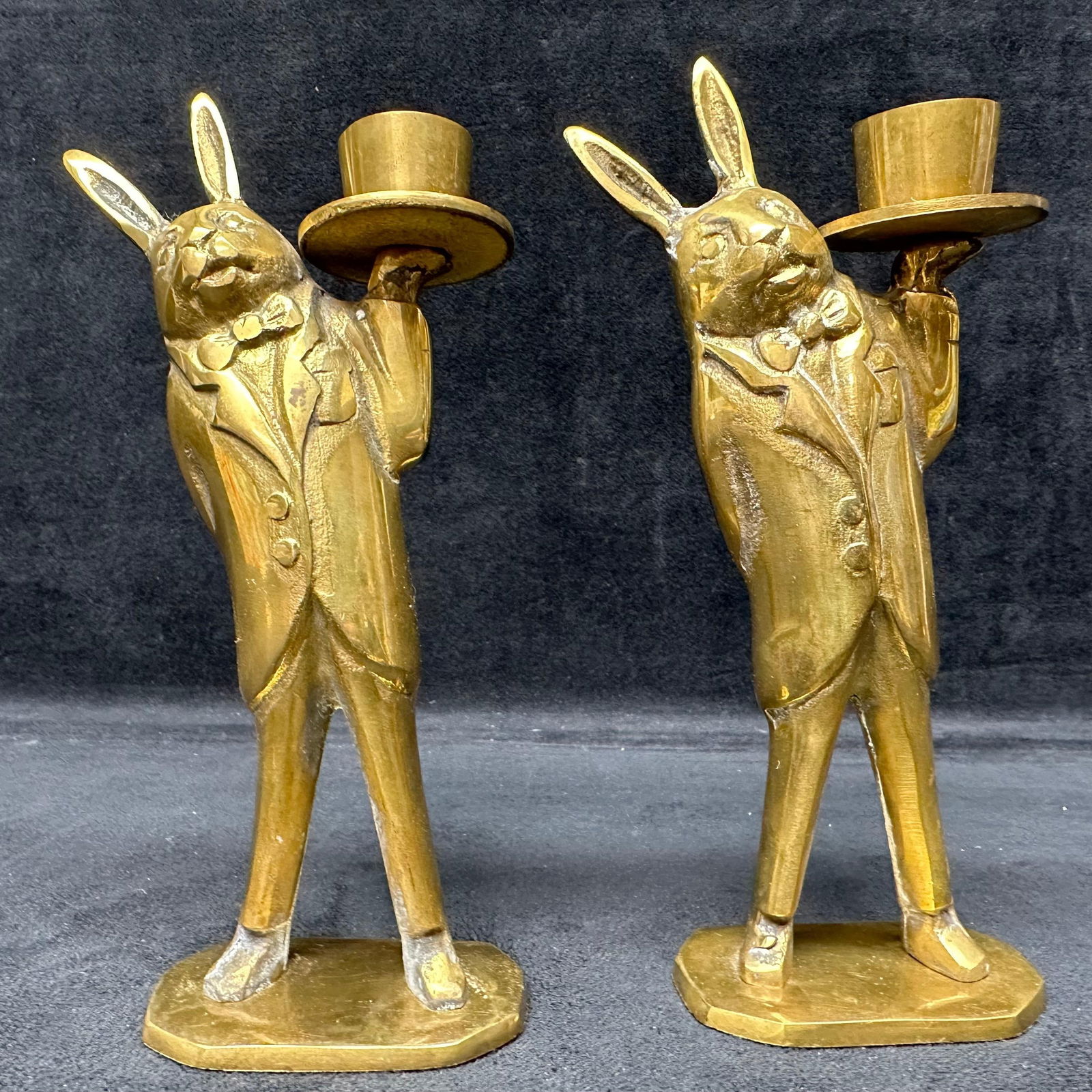 Pair of Vintage Brass Rabbit Butler Candlestick Holders Made in Korea: Pair of standing cast brass rabbit candlestick holders, each rabbit dressed in a formal suit and bow tie while holding a top hat designed to hold a taper candle. Nicely weighted with a polished brass