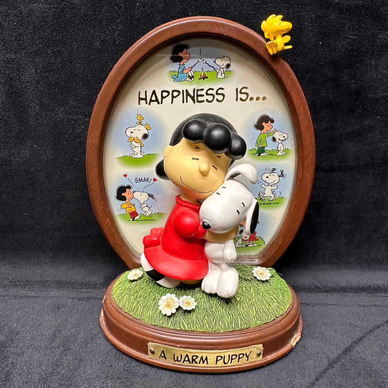 Peanuts Snoopy Happiness Is A Warm Puppy Danbury Mint Figure: Collectible figurine features Lucy Van Pelt hugging Snoopy, with an oval backdrop depicting various other "Peanuts" comic strip panels. Figurine crafted from resin and hand-painted. Minor chip