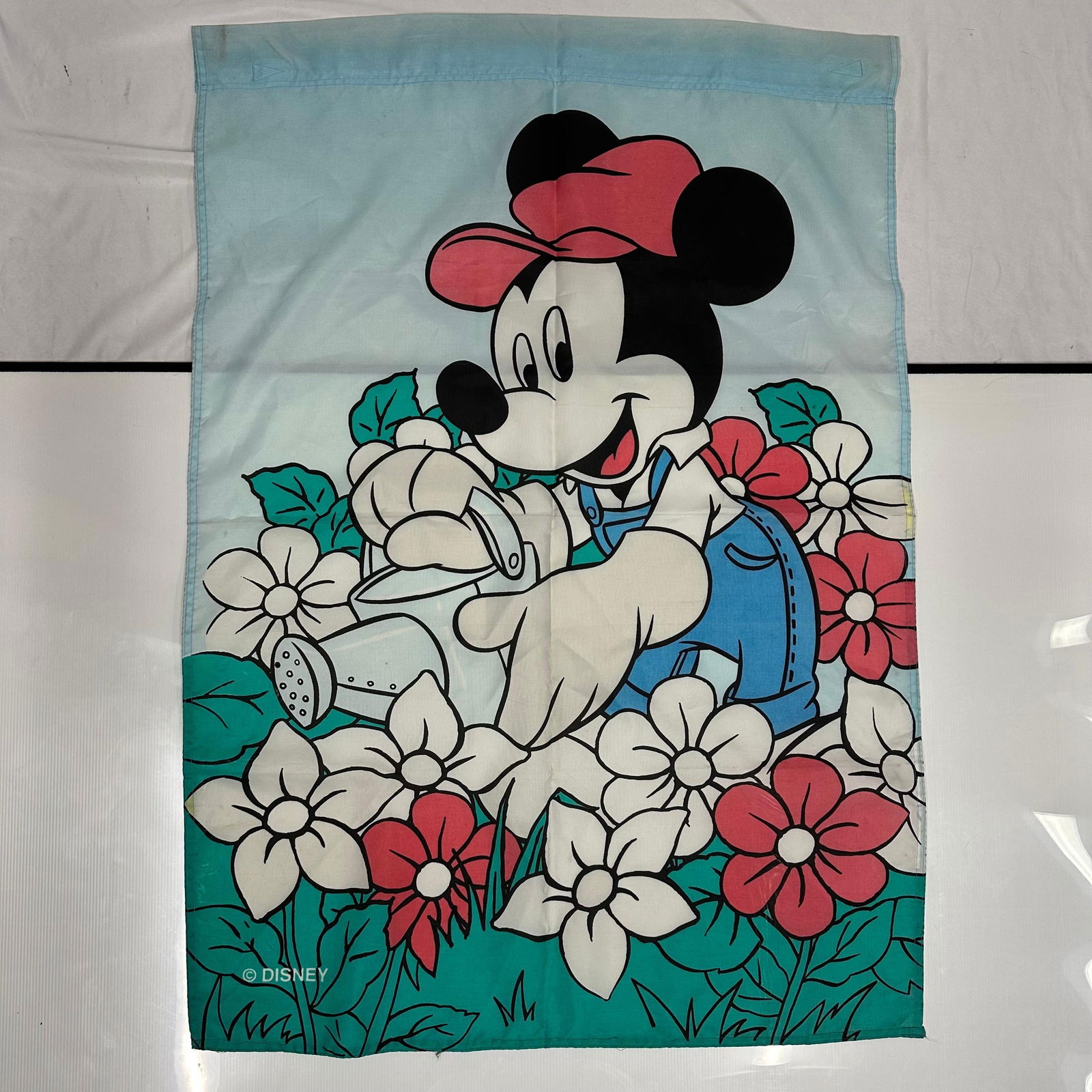 Mickey Mouse Disney Outdoor Home Garden Decorative Fabric Flag: Outdoor garden flag featuring Mickey Mouse watering flowers, produced by Disney. Printed fabric flag with stitched edges, designed for outdoor garden or yard display. The artwork shows Mickey in a flo