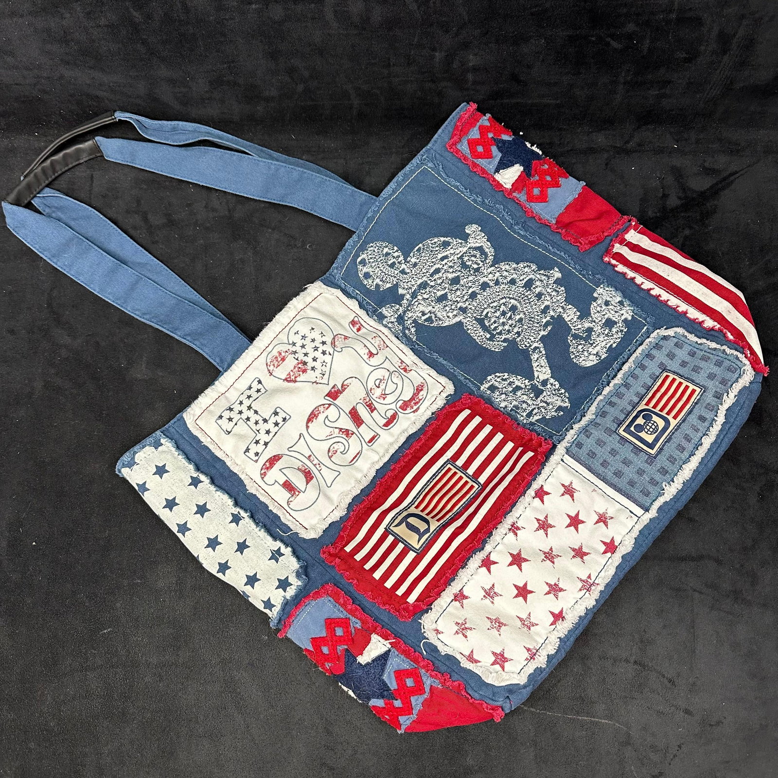 Disney Parks Patchwork Tote Bag with Patriotic Mickey Mouse Design: Disney Parks branded fabric tote bag featuring a patchwork design with red, white, and blue motifs, including Mickey Mouse graphics, stars, stripes, and I Love Disney text. Constructed of mixed textil