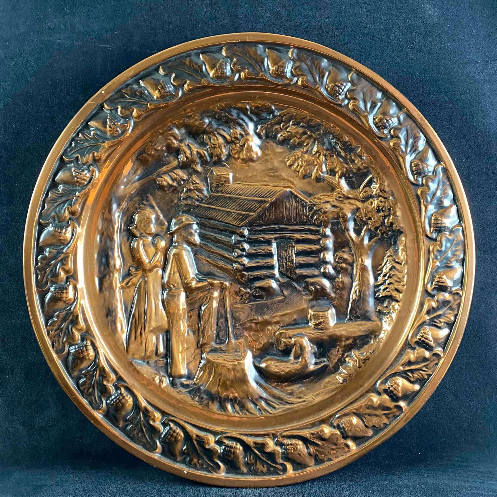 20" Decorative Copper Plate: 20" Decorative Copper Plate Decorative copper plate with relief design and brass loop for candleholder. Shows a couple outside of a log cabin. In good condition with no known damage. Approximate