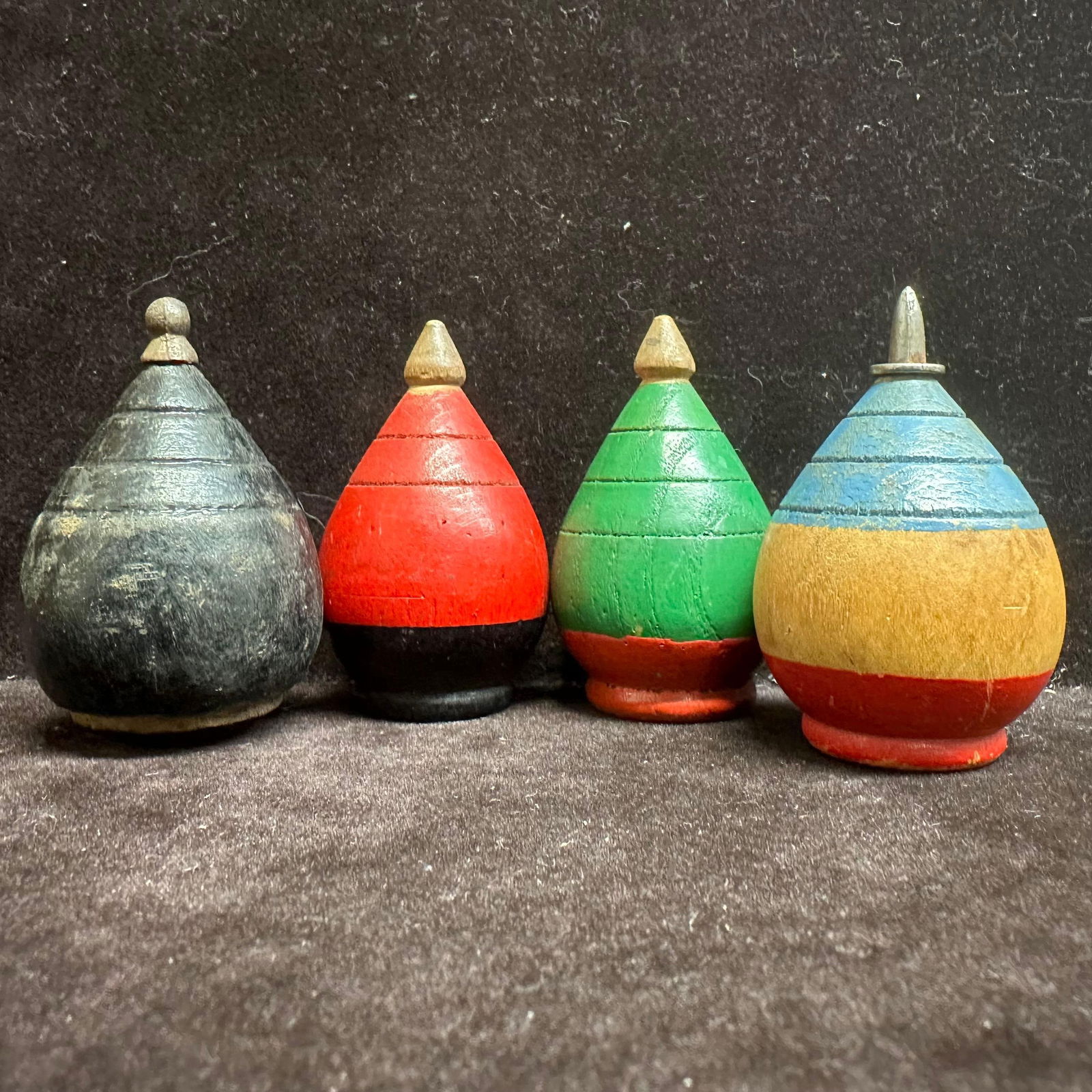 Group of Four Vintage Painted Wooden Spinning Tops: Group of four hand-painted wooden spinning tops in assorted colors and forms. Likely mid-20th-century examples. Two have metal tips. Each shows age-appropriate wear, surface wear, and paint loss consi