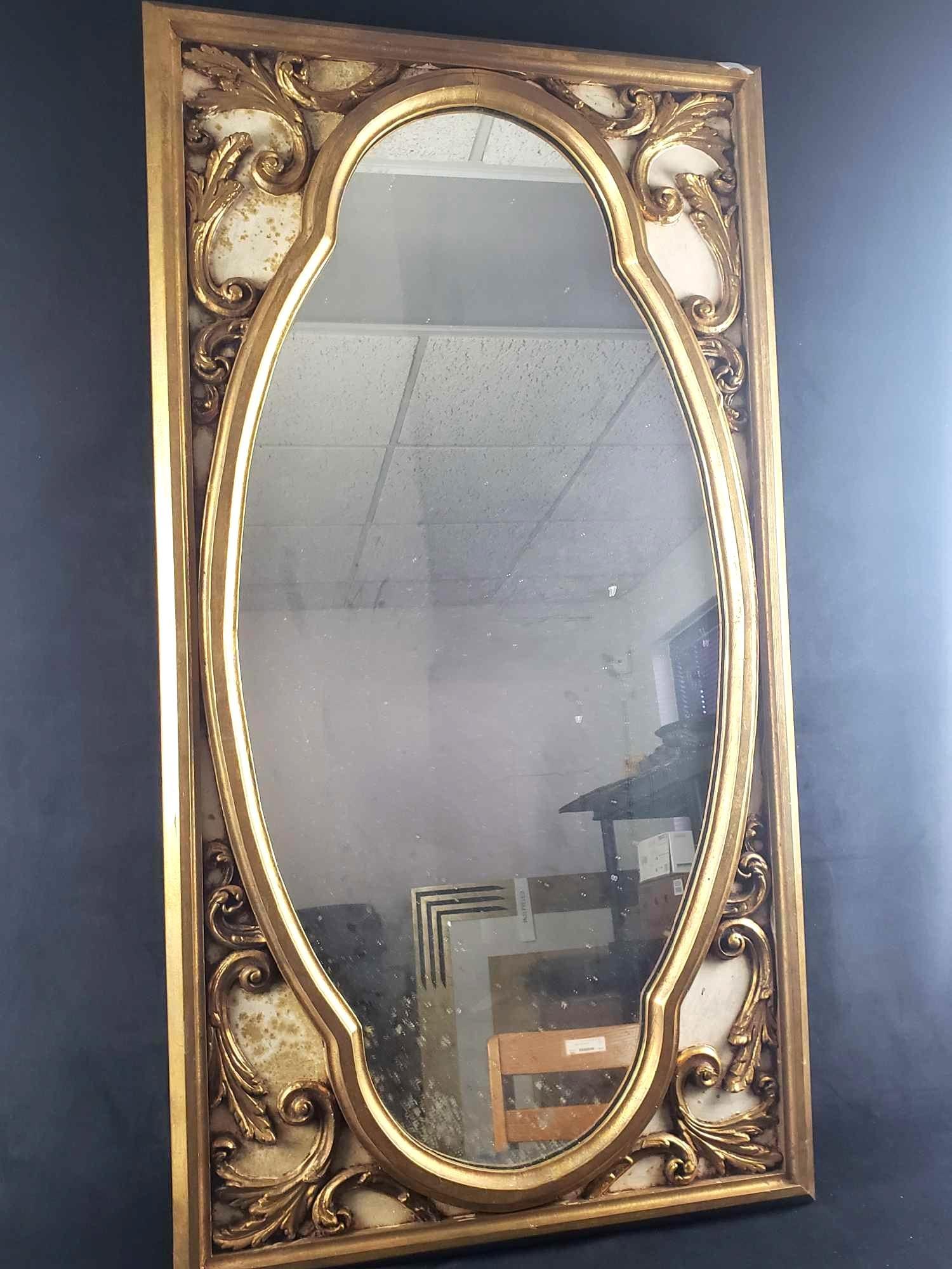 Gold Framed Ornate Mirror: Gold Framed Ornate Mirror. This mirror is in good to fair condition. The mirror is oval and surrounded by a gold wooden frame. The areas around the decoration show signs of use which needs to be
