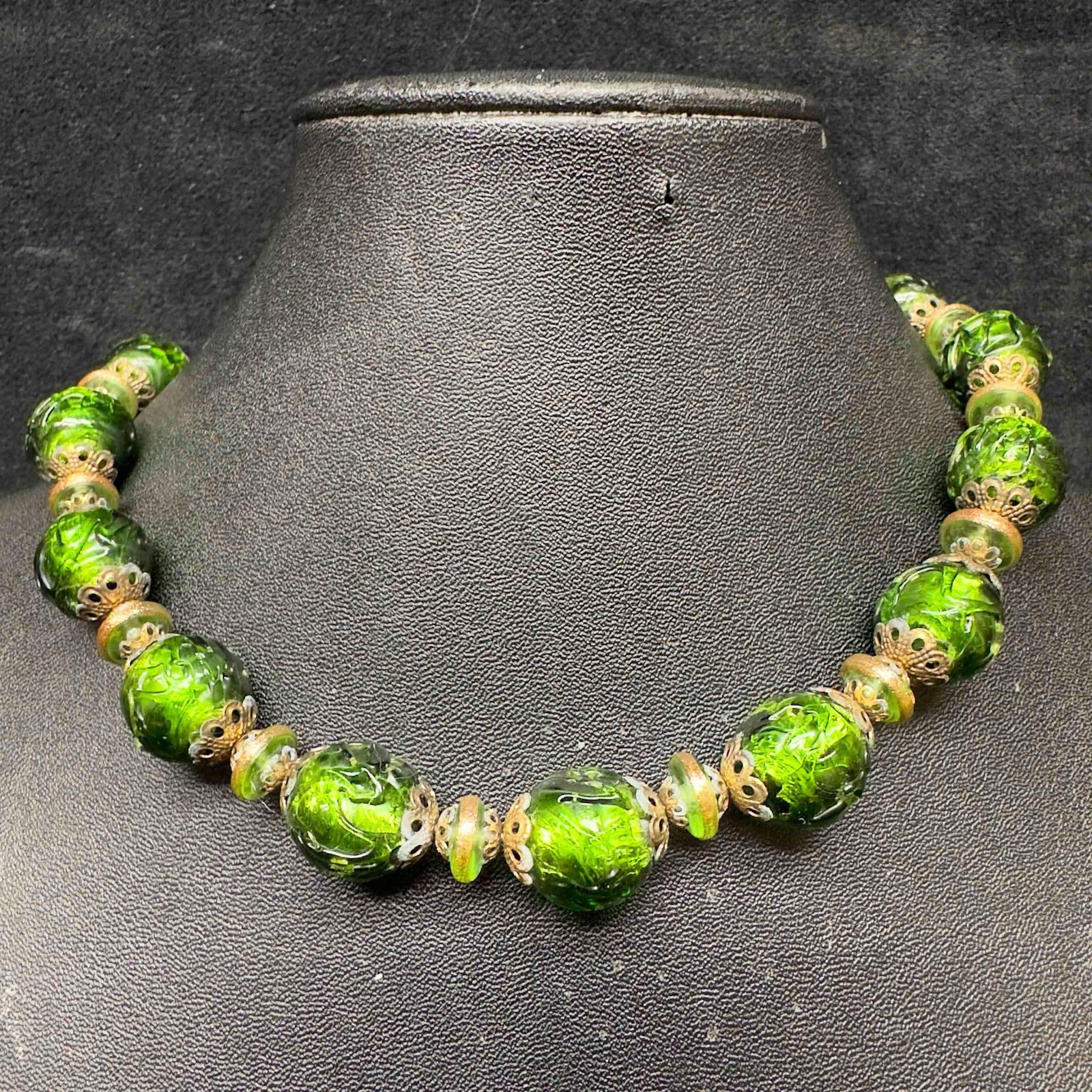 Murano Venetian Lamp Work Art Glass Dark Green Beaded Necklace C73: Murano Venetian Lamp Work Art Glass Dark Green Beaded Necklace C73. Necklace with green glass beads with beautiful designs on each. The necklace features gold accents. The necklace features a barrel c