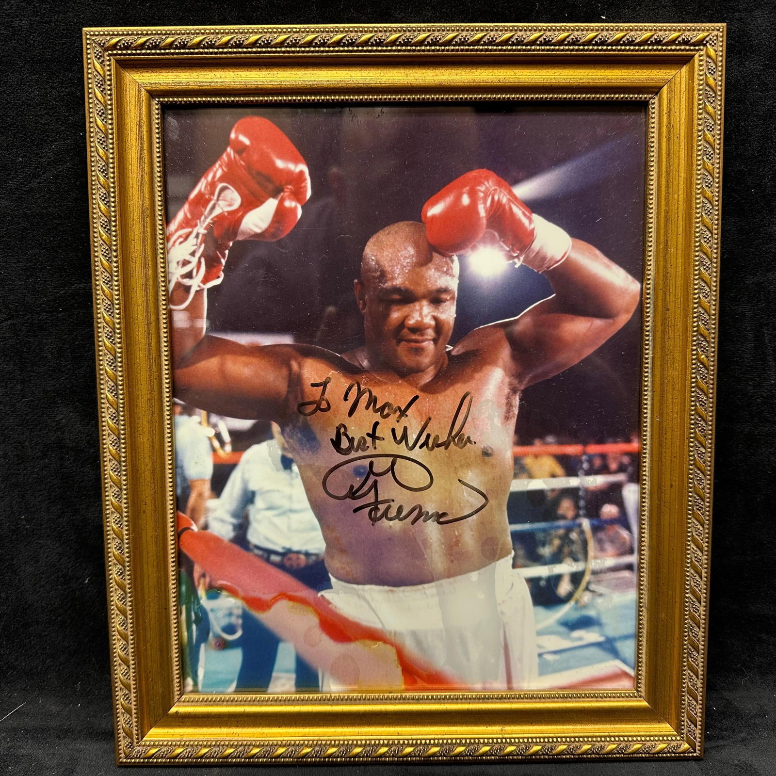 Framed Autographed Photograph of George Foreman Signed To Max Best Wishes: Color photographic print depicting heavyweight boxing champion George Foreman in the ring with raised gloves, signed in black marker across the image with the inscription To Max, Best Wishes and signa