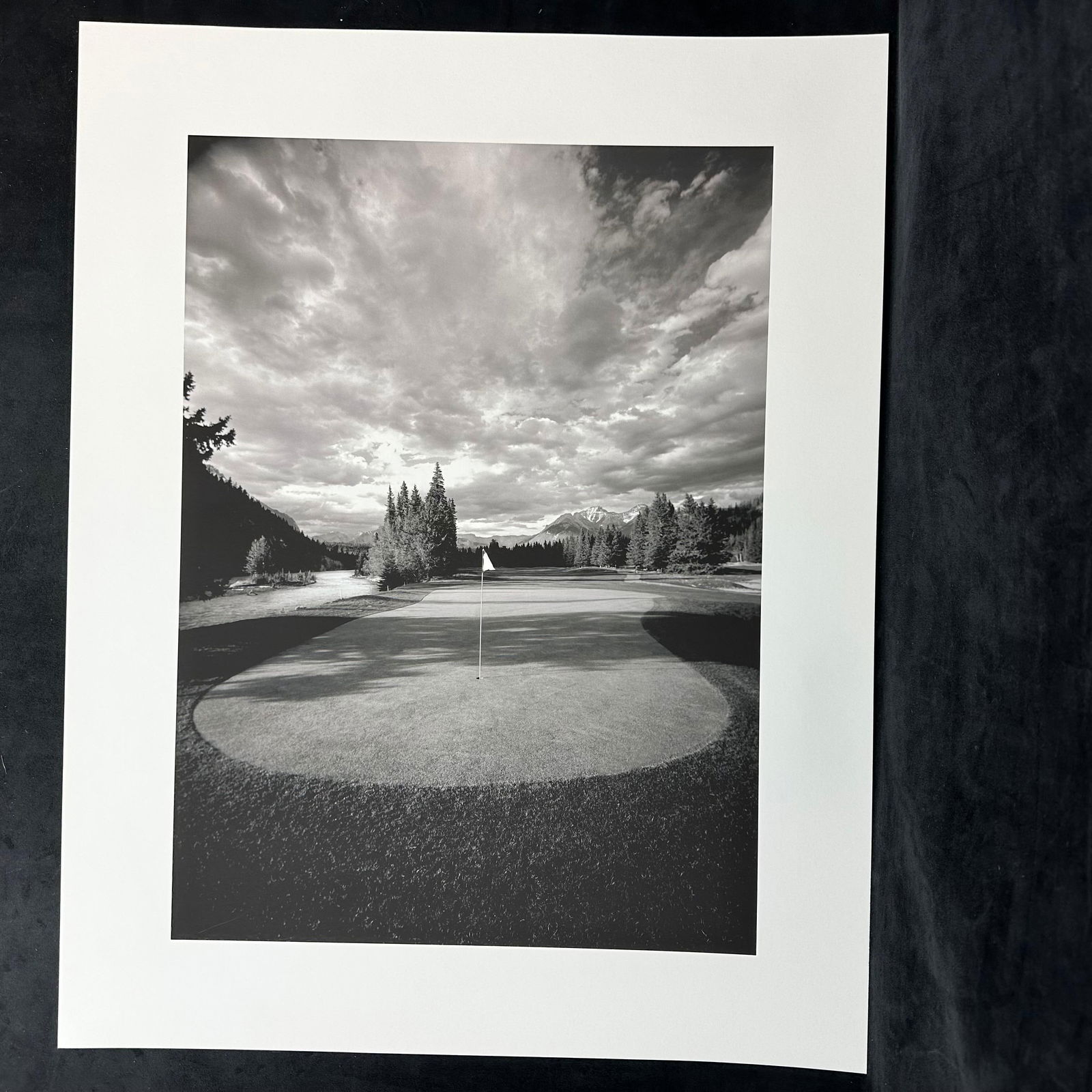 Black and White Fine Art Photograph Print Golf Course Landscape with Mountain View: Black and white fine art photograph, ink jet print featuring a golf course green framed by a dramatic sky, distant mountains, and evergreen trees. Unmarked on reverse. This item is in pre-owned,