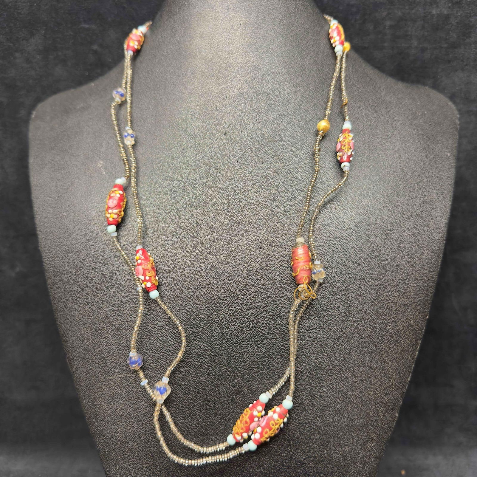 Venetian Murano Lamp Work Glass Art Red Beaded Long Necklace Plastic Bead D8: Venetian Murano Lamp Work Glass Art Red Beaded Long Necklace Plastic Bead D8. Necklace with red colored glass beads with a beautiful design on each. The necklace features pink colored and gold toned a