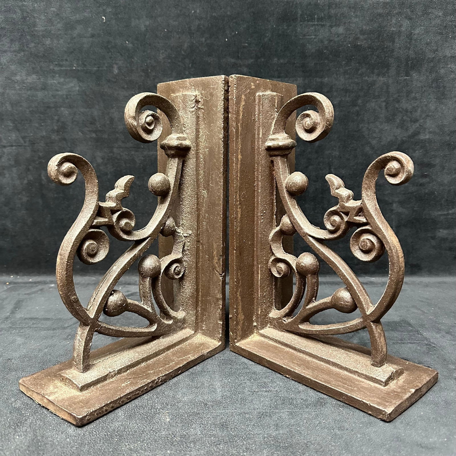 Pair of Cast Iron Scrollwork Bookends: Pair of heavy cast iron bookends with ornate scrollwork and ball accent design. Sturdy construction suitable for supporting books on a shelf or mantel. Light wear consistent with the display. These it