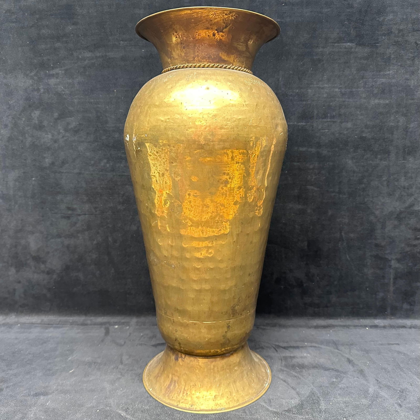 Vintage Hand Hammered Brass Vase with Grape Motif Accents: Tall vintage hand-hammered brass vase featuring a flared rim, tapered body, and applied rope-style band with hanging grape cluster accents. Shows age-related patina, surface wear, and oxidation throug