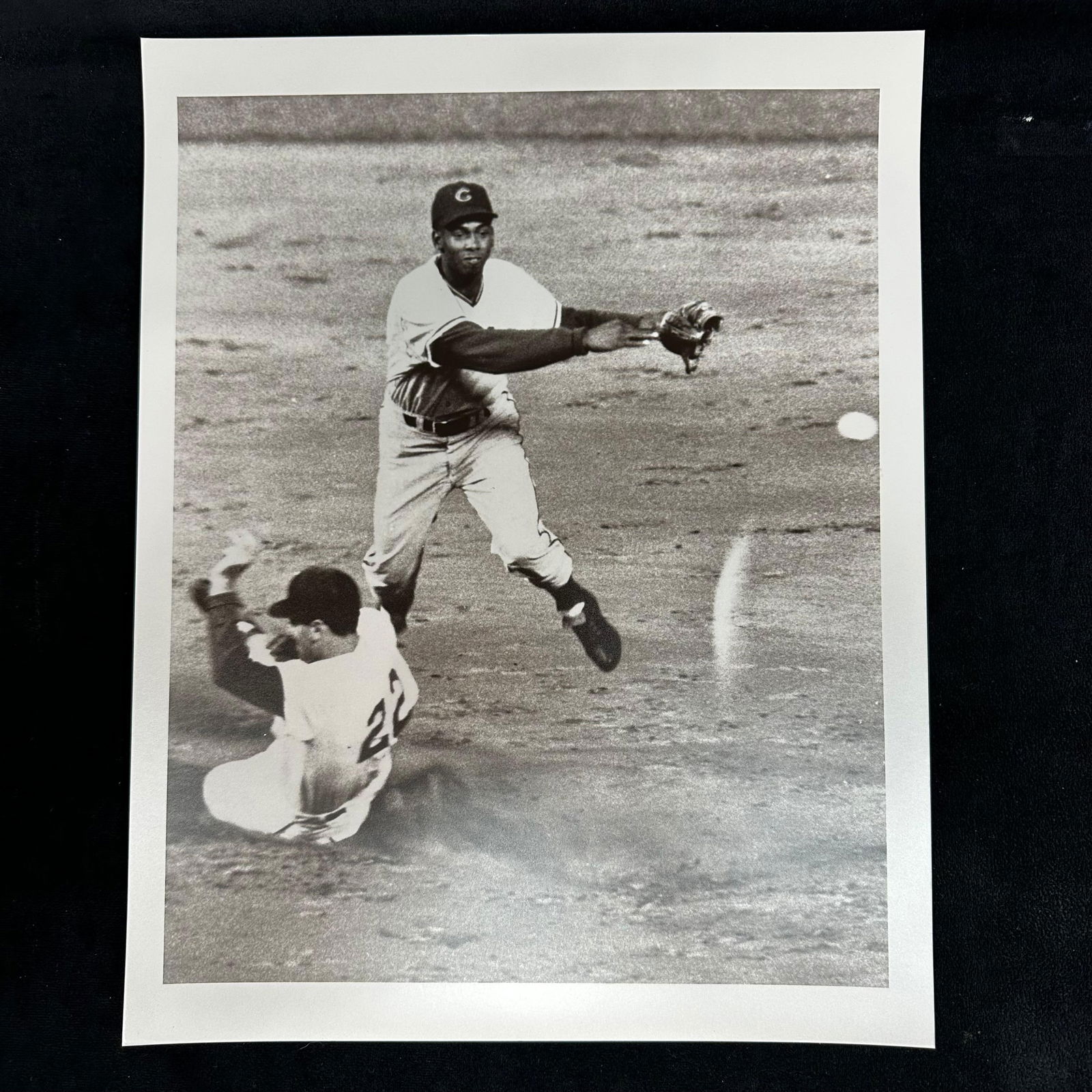 Black and White Baseball Action Analog Photo Print Infield Double Play Scene #2: Black and white analog photo print depicting an infield double play attempt. One player is captured mid-air, throwing the ball as a runner slides beneath. Blank reverse side. This item is in pre-owned