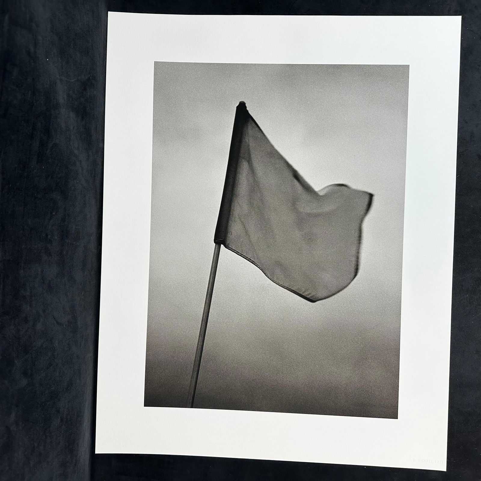 Michael Faye Embossed Black and White Fine Art Photograph Print Golf Flag: Black and white fine art photograph by Michael Faye, featuring a golf course flag gently waving in the wind against a minimalist sky. Embossed in the lower right corner Michael Faye. Printed on high-q