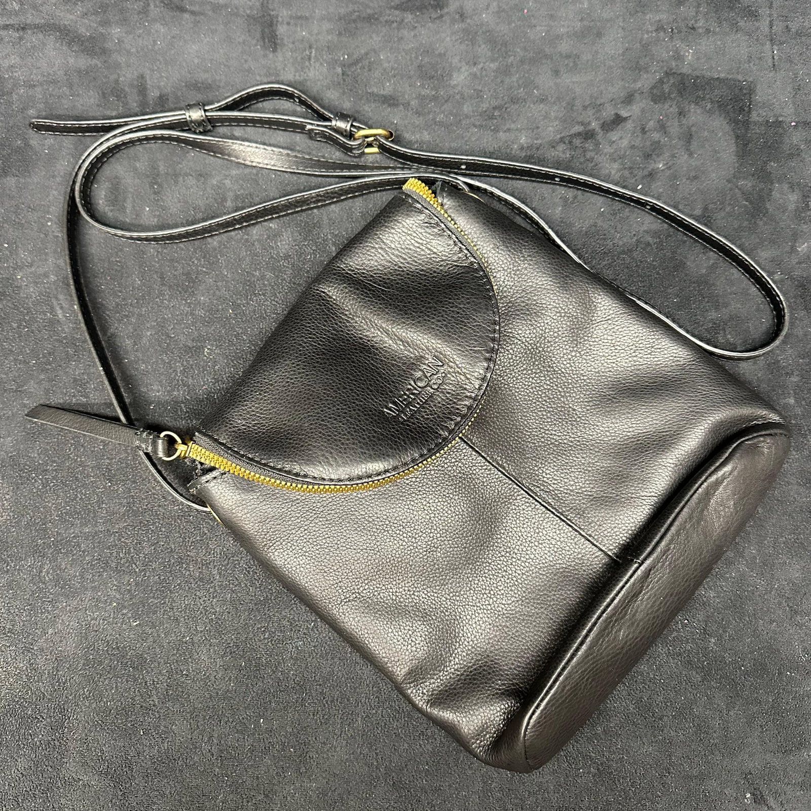 American Leather Co. Black Pebbled Leather Crossbody Shoulder Bag: American Leather Co. black pebbled leather crossbody shoulder bag. Features a curved front zippered pocket with embossed American Leather Co. logo, gold-tone hardware, and adjustable leather shoulder