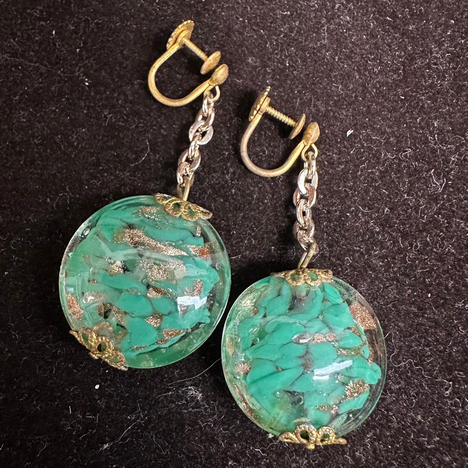 Murano Venetian Art Glass Lamp Work Green Circle Copper Accent Earrings C49: Earrings with green colored glass beads with beautiful designs on each. The earrings feature copper accents. The earrings feature a screw back clip on clasp fastener closure. These items are in good