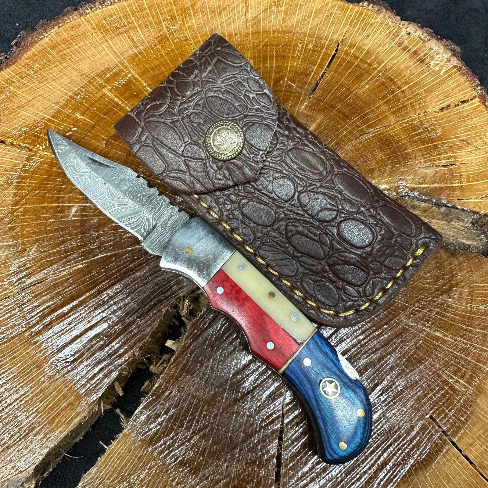 American Themed MHS Cutlery Steel Folded Blade Pocket Knife with Sheath Q75: Folding blade pocket knife by MHS Cutlery featuring a layered patterned steel blade and decorative spine work. The handle has a contoured, red, white, and blue American-themed wood/resin-style grip wi