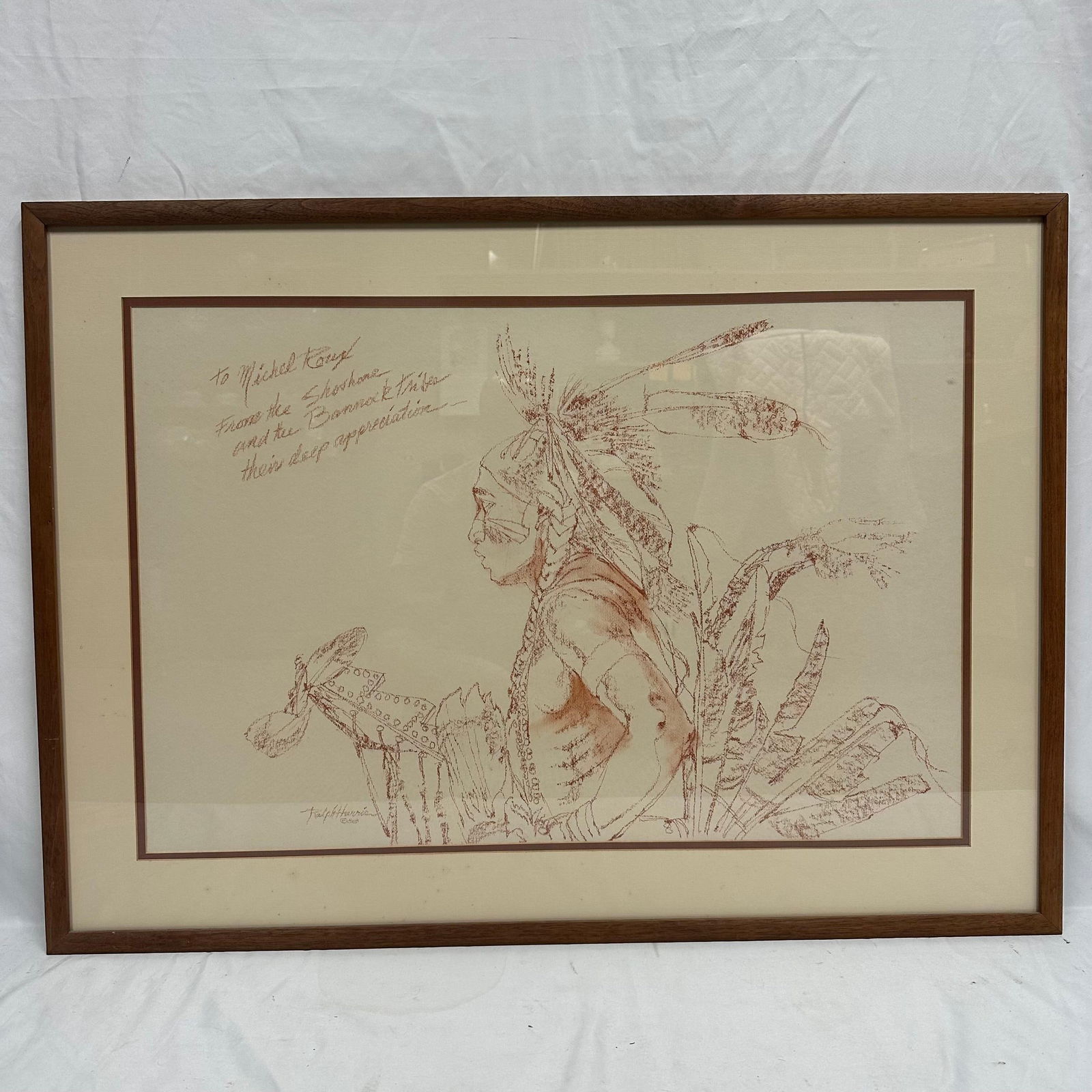 Ralph Harris Shoshone and Bannock Warrior Signed Artwork with Dedication: Framed artwork by artist Ralph Harris, depicting a Native American warrior in detailed line work with a feathered headdress and traditional regalia. The piece includes a handwritten dedication: “To
