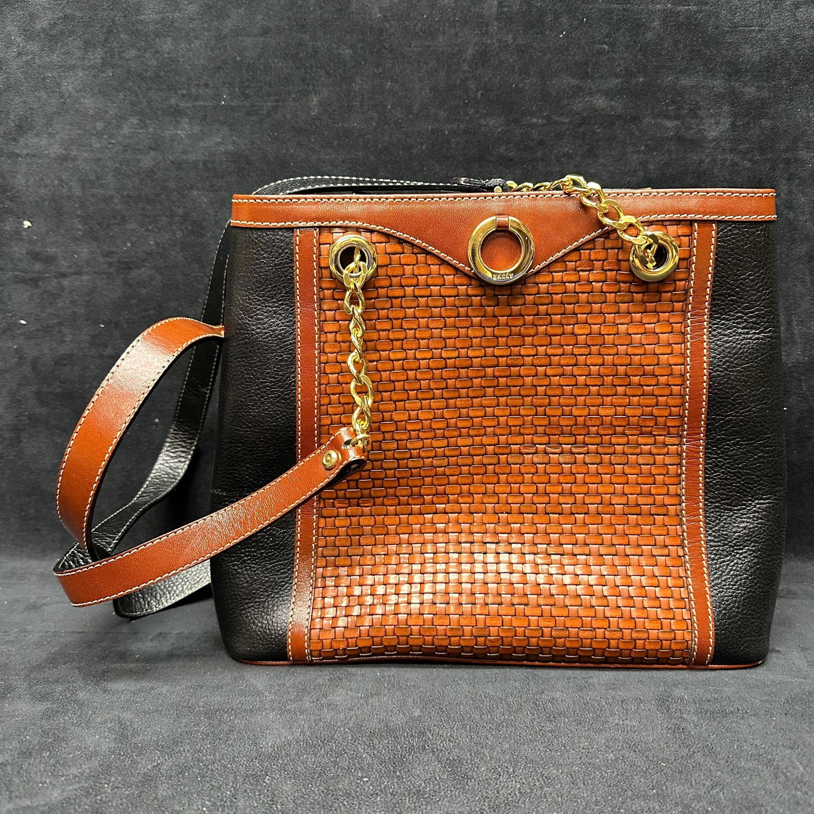 Bally Woven Leather Tote Bag with Chain Strap Black and Brown Vintage: Designer tote bag by Bally featuring a woven leather front panel framed by smooth brown leather trim and black grained leather sides. The bag is accented with gold-tone hardware, including chain shoul