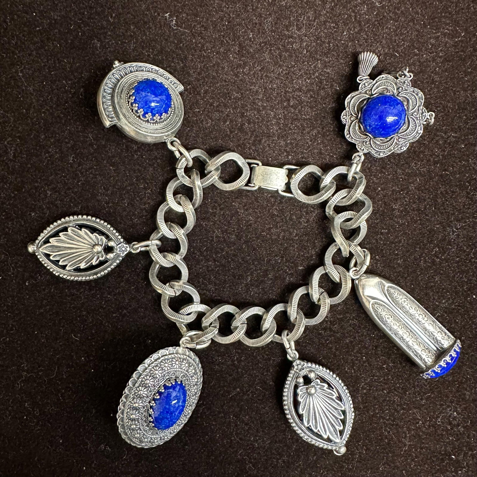 Vintage Napier Silver-Tone Charm Bracelet with Blue Cabochon Charms: Vintage charm bracelet by Napier, featuring a heavy silver-tone link chain with multiple ornate dangling charms. The bracelet includes decorative oval and round settings accented with vivid blue caboc
