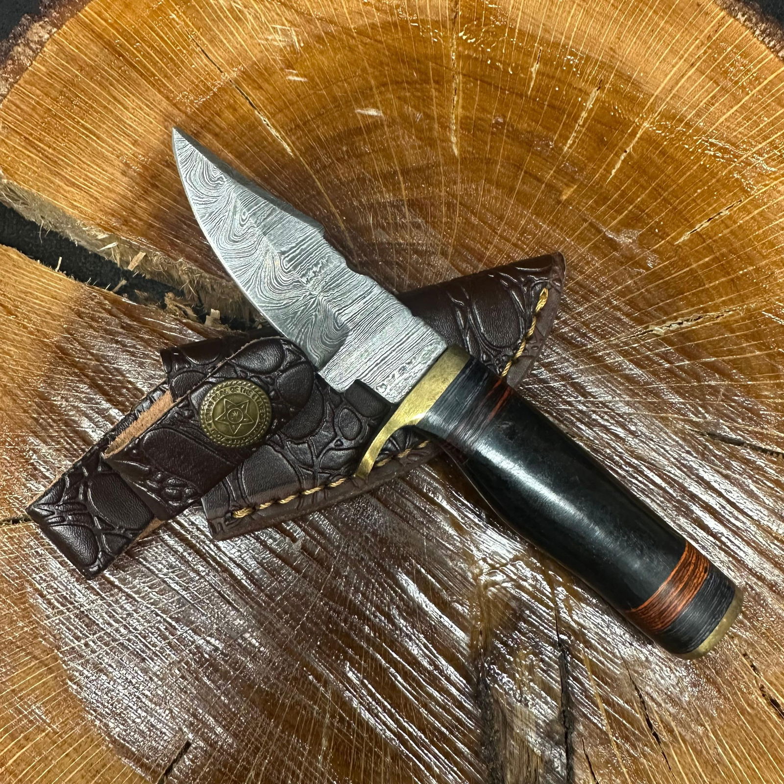 Small Fixed Blade Knife MHS Cutlery Orange Band Black Handle R33: Fixed blade knife by MHS Cutlery featuring a textured steel blade and decorative spine work. The handle has a contoured, black epoxy resin/wood-style grip with metal mosaic accents. Includes a fitted