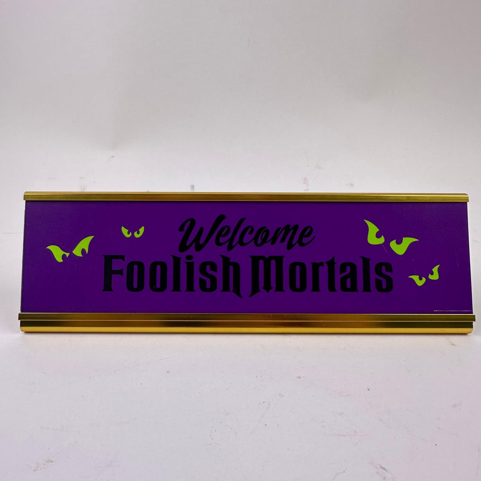 Foolish Mortals Haunted Mansion Desk Decor Disney Table Plaque: Disney spirited office decor! This metal desk nameplate, inspired by The Haunted Mansion attraction, is an eye-catching accent that sets the tone for entertaining with the legendary, Welcome, foolish