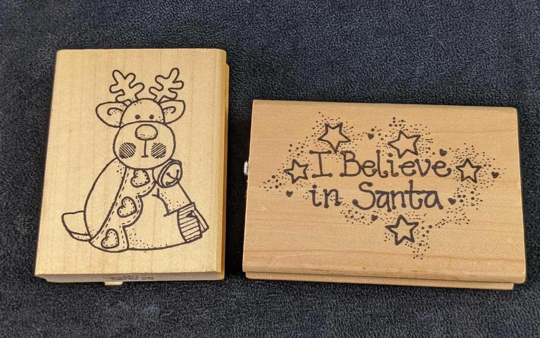 Two Fun Wooden Christmas Stamps By Imagine That: This lot consists of: (1) Blushy Reindeer Stamp. (1) "I Believe In Santa" Stamp. Both are made by "Imagine That" and are in a good, used condition with dried ink on the stamp. They a