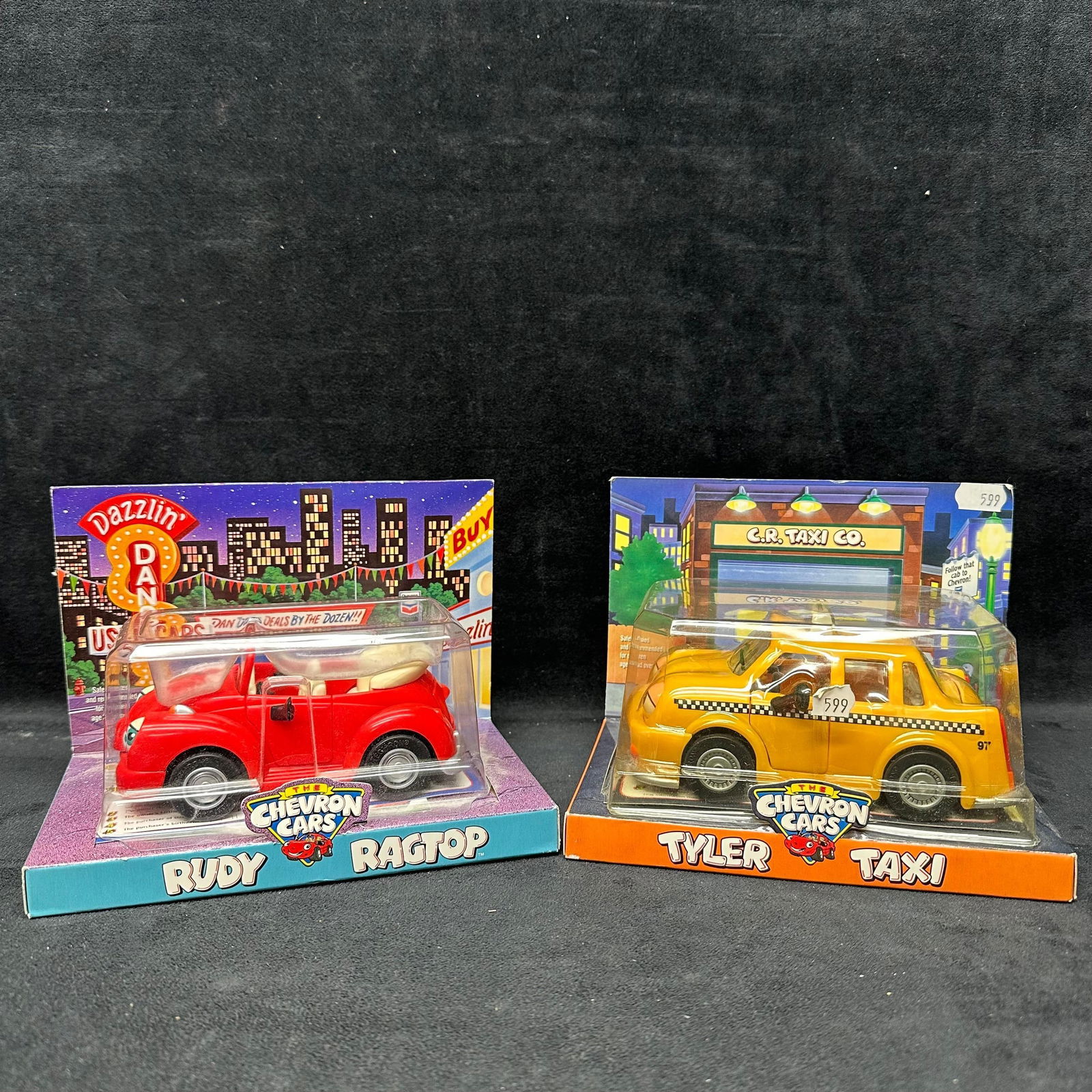 Chevron Cars Rudy Ragtop and Tyler Taxi Toy Cars Like New Pair: Pair of Chevron Cars character vehicles, including Rudy Ragtop (red convertible) and Tyler Taxi (yellow taxi). Both are die-cast with plastic components and remain sealed in their original retail