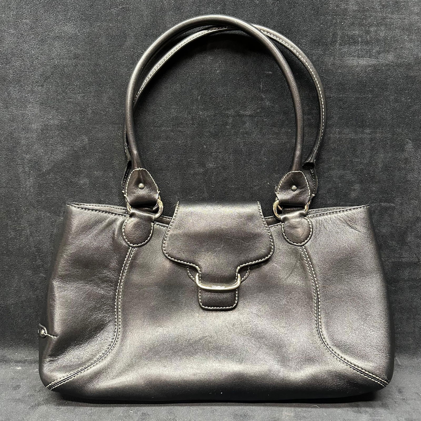 Cole Haan Black Leather Shoulder Tote Bag: Black leather shoulder tote by Cole Haan featuring dual rolled handles and a front flap accent with polished metal hardware stamped Cole Haan. Structured silhouette with contrast stitching and side