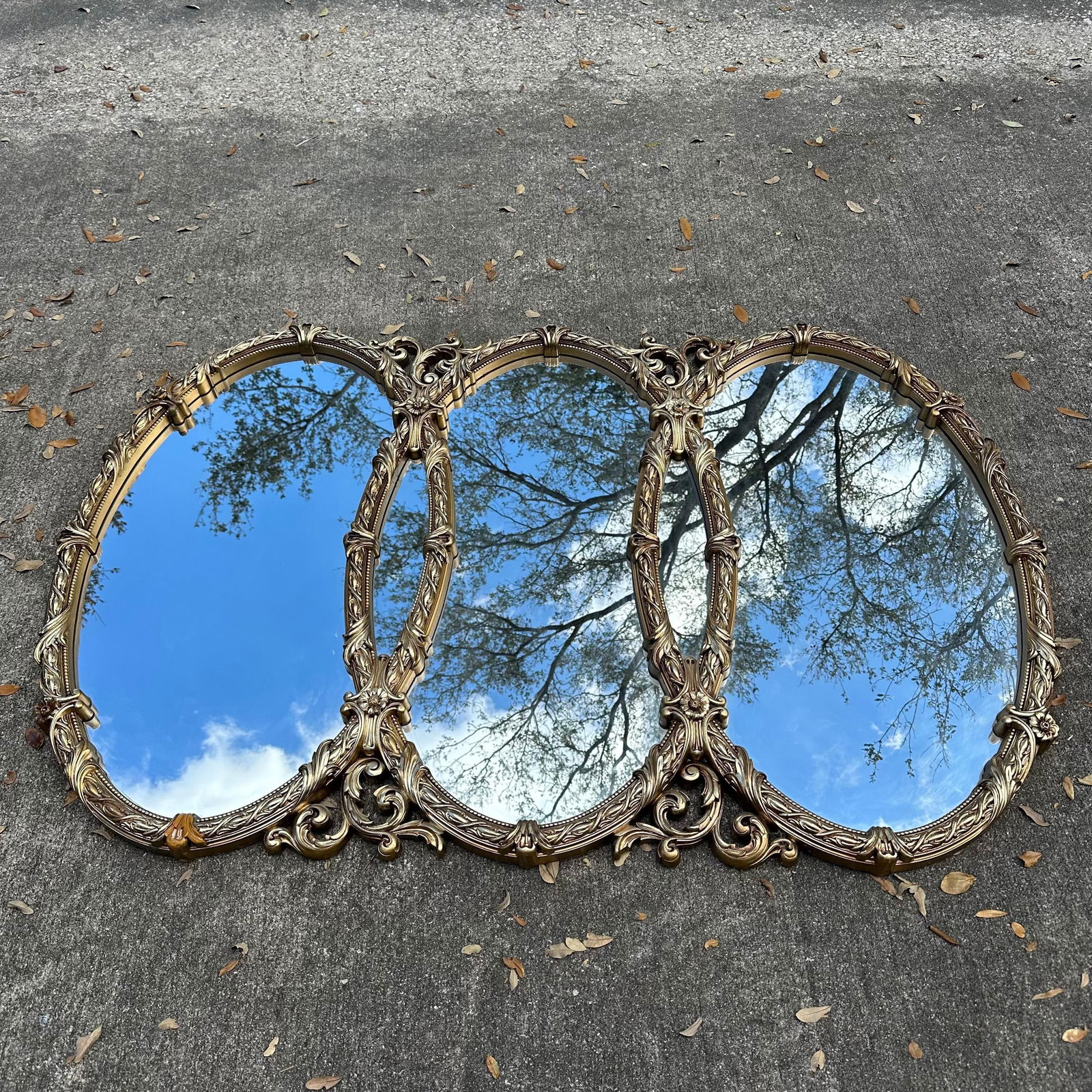Vintage Bassett Mirror Co. Triple Oval Gold Gilt Wall Mirror: Large vintage triple-panel wall mirror by Bassett Mirror Co., Bassett, Virginia. Features three connected oval mirrors within an ornate gold-tone molded frame with scrolling acanthus leaf and floral d
