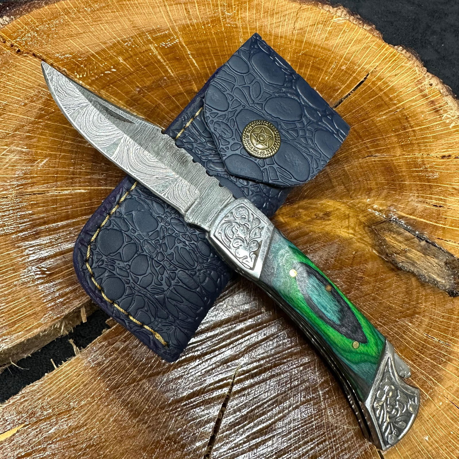 MHS Cutlery Steel Folded Blade Pocket Knife Green and Blue Handle Q82: Folding blade pocket knife by MHS Cutlery featuring a layered patterned steel blade and decorative spine work. The handle has a contoured, wood/resin-style grip with metal mosaic pin accents.