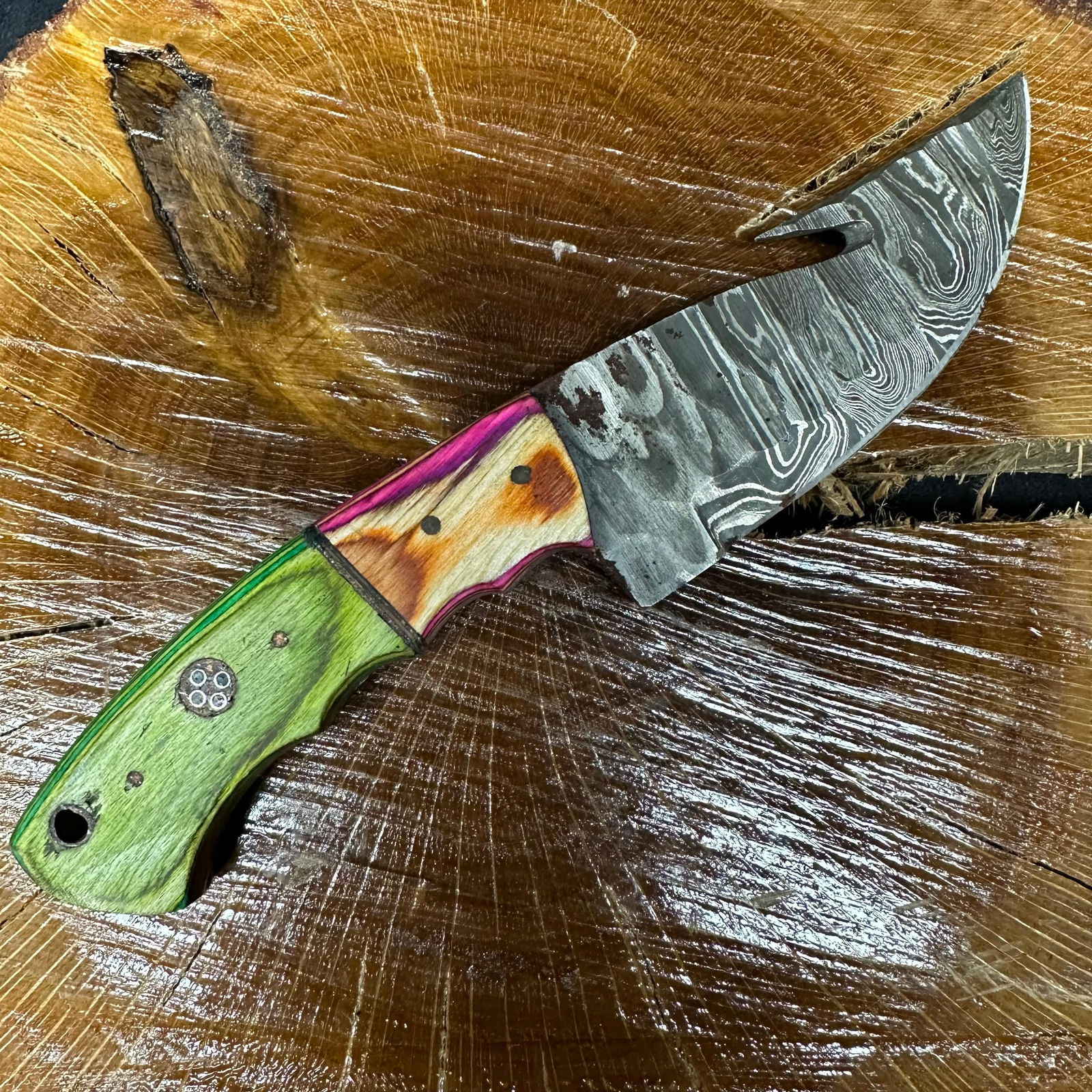 MHS Cutlery Fixed Blade Knife Green Pink Wooden Handle Rusting P42: Fixed blade knife by MHS Cutlery featuring a textured steel blade and decorative spine work. The handle has a contoured, multi-colored resin-style grip with metal mosaic pin accents and a lanyard hole