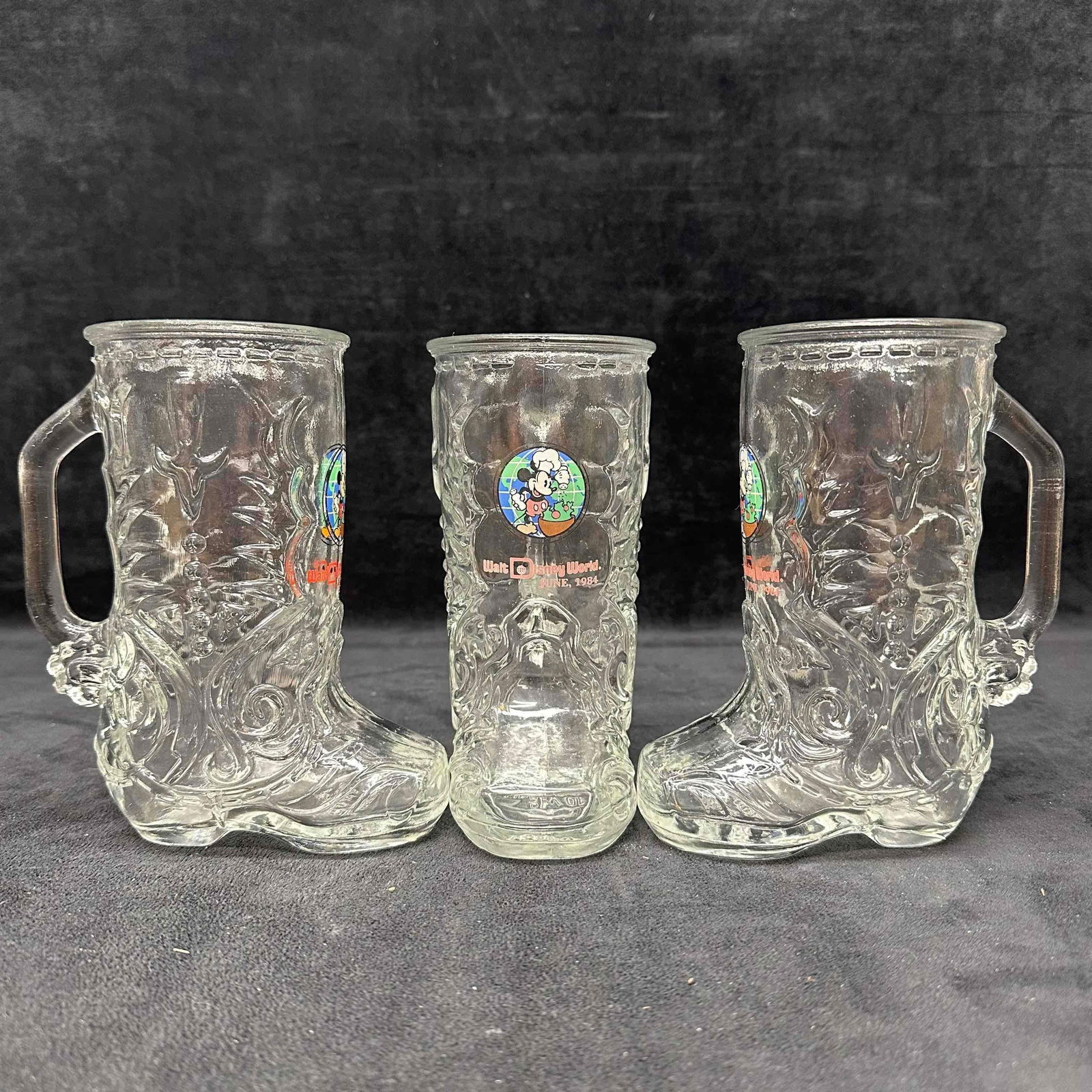 Libbey Glass Walt Disney World 1984 Boot-Shaped Mug Set of 3 Mugs: Set of three clear glass mugs shaped like cowboy boots, each featuring colorful Mickey Mouse chef graphic with "Walt Disney World, June 1984" text. Made by Libbey Glass, USA. Heavy embossed gl