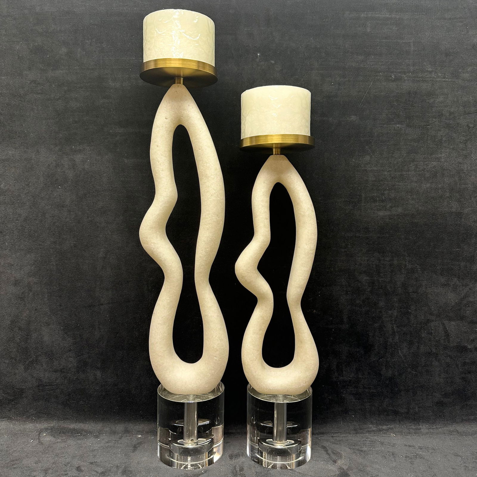Modern Sculptural Stone Composite and Crystal Glass Candle Holders with Brass Accents Pair: Contemporary pair of sculptural candle holders featuring abstract, flowing composite stone-form bodies mounted on clear crystal glass bases. Each is topped with a brass-tone metal candle cup and inclu