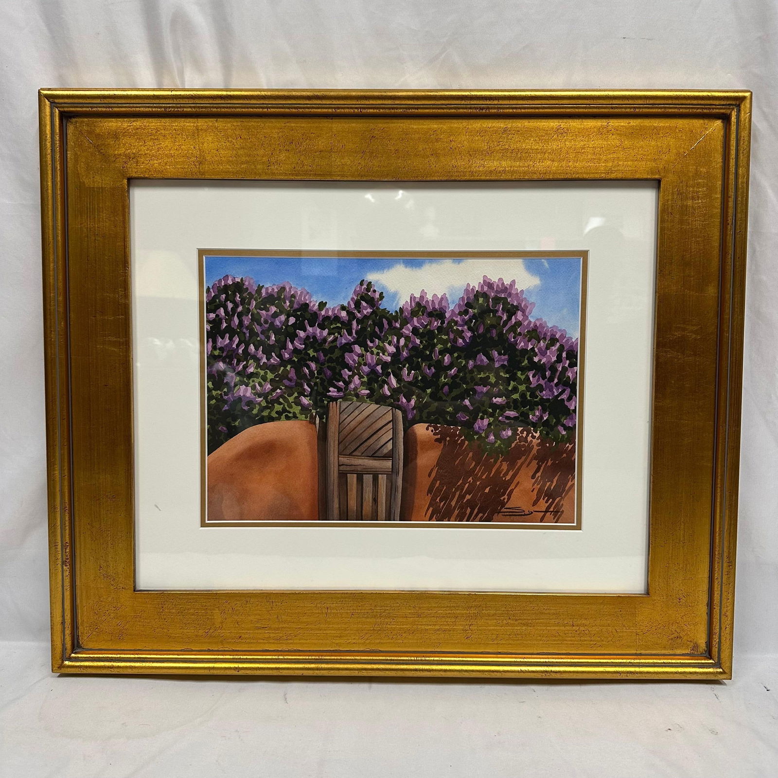 Shirley Lynn Watercolor Southwestern Gate Signed Framed: Framed watercolor painting by artist Shirley Lynn depicting a Southwestern adobe wall and wooden gate with vibrant purple flowering shrubs against a bright blue sky. Signed in the lower right. Present