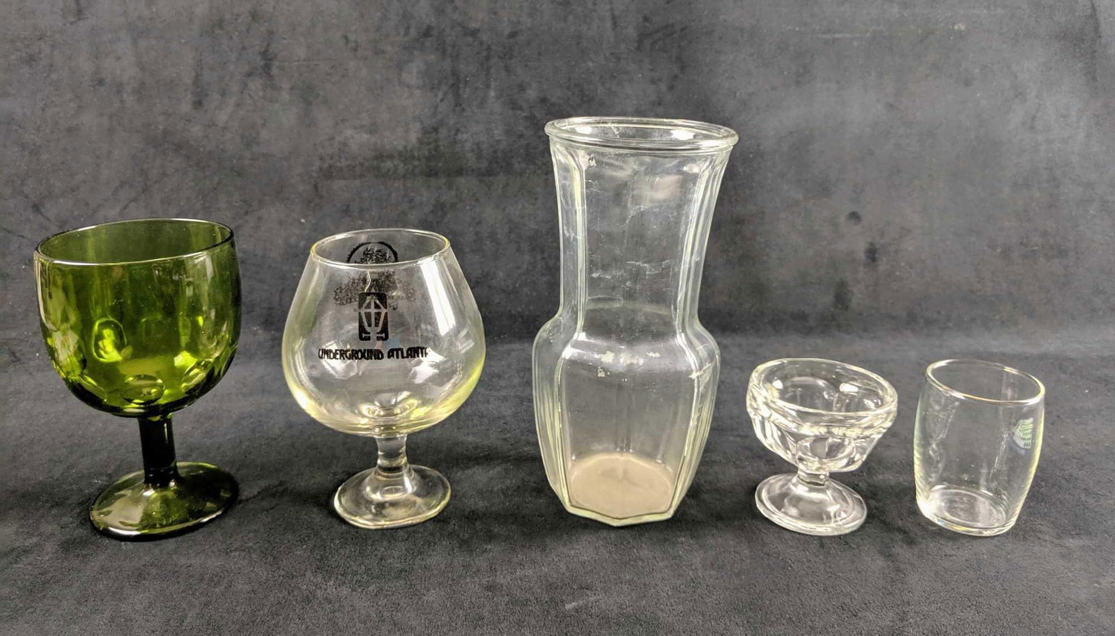 Set Of Miscellaneous Glassware: This is an group of random glasses. From a fun party glass from closed "Atlanta Underground" shopping district to a glass drinking chalice. These measure from left to right. 3' L 4'W 6'H 5'