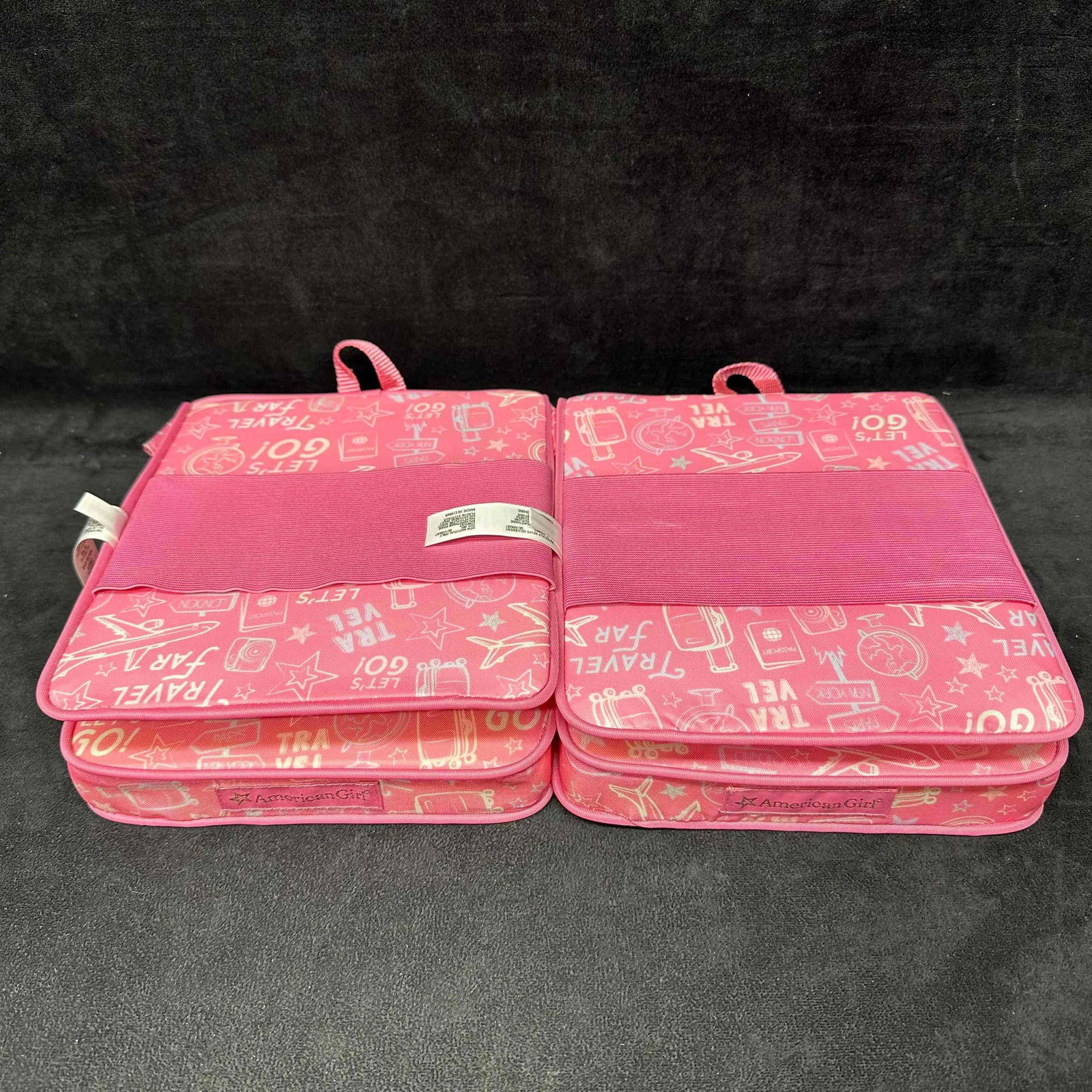 American Girl Doll Pink Love to Travel Seat Chair Set of 2: Pair of American Girl doll travel seats in bright pink with playful “Let’s Go!” and travel-themed designs. Each folds open to create a compact chair setup for dolls and includes elastic