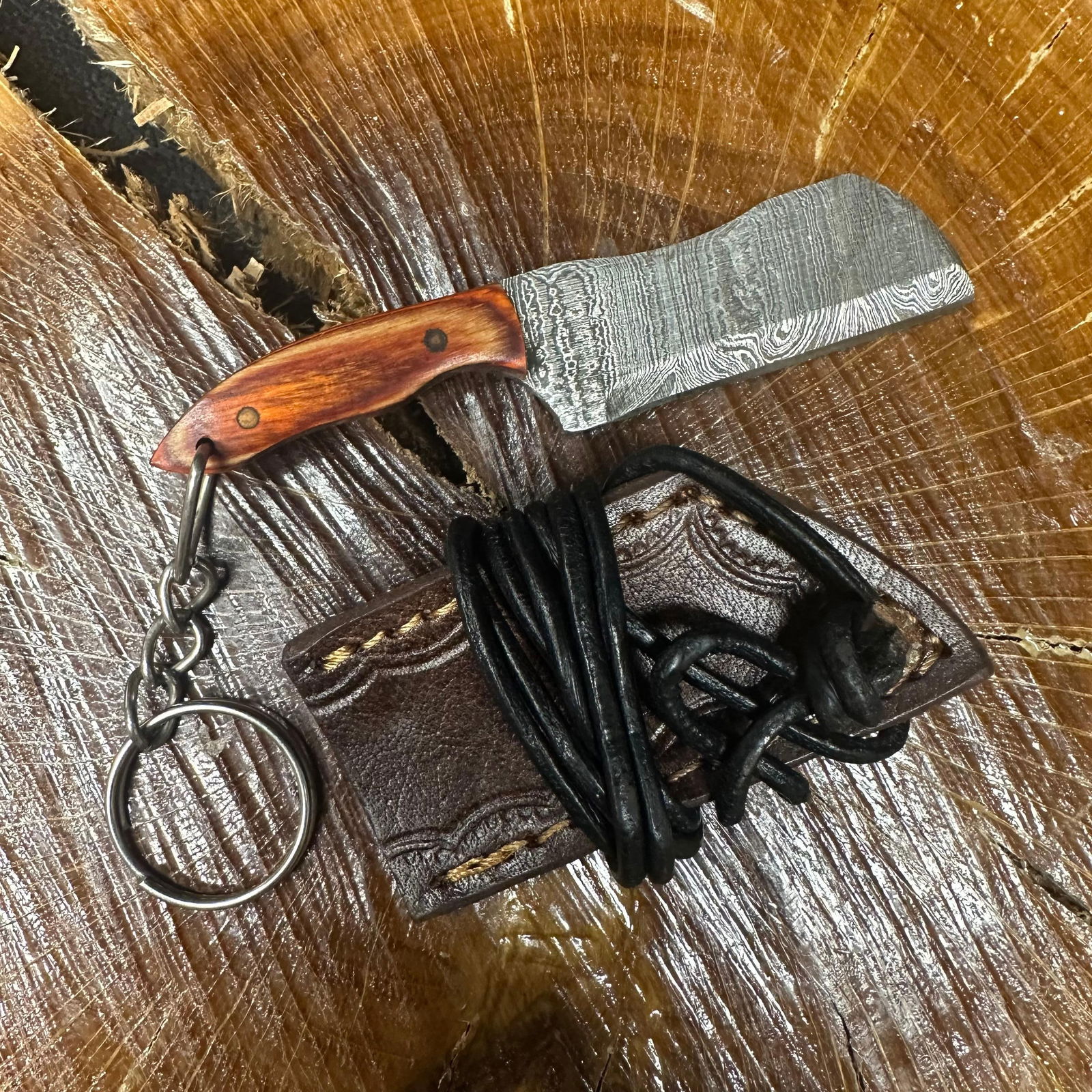 MHS Cutlery Keychain Cleaver Style Blade Knife With Leather Case Necklace R42: Small key chain-sized fixed-blade knife featuring a patterned steel blade and a compact epoxy-resin/wood brown/orange-tone handle secured with brass pins. Includes a fitted brown leather sheath with s
