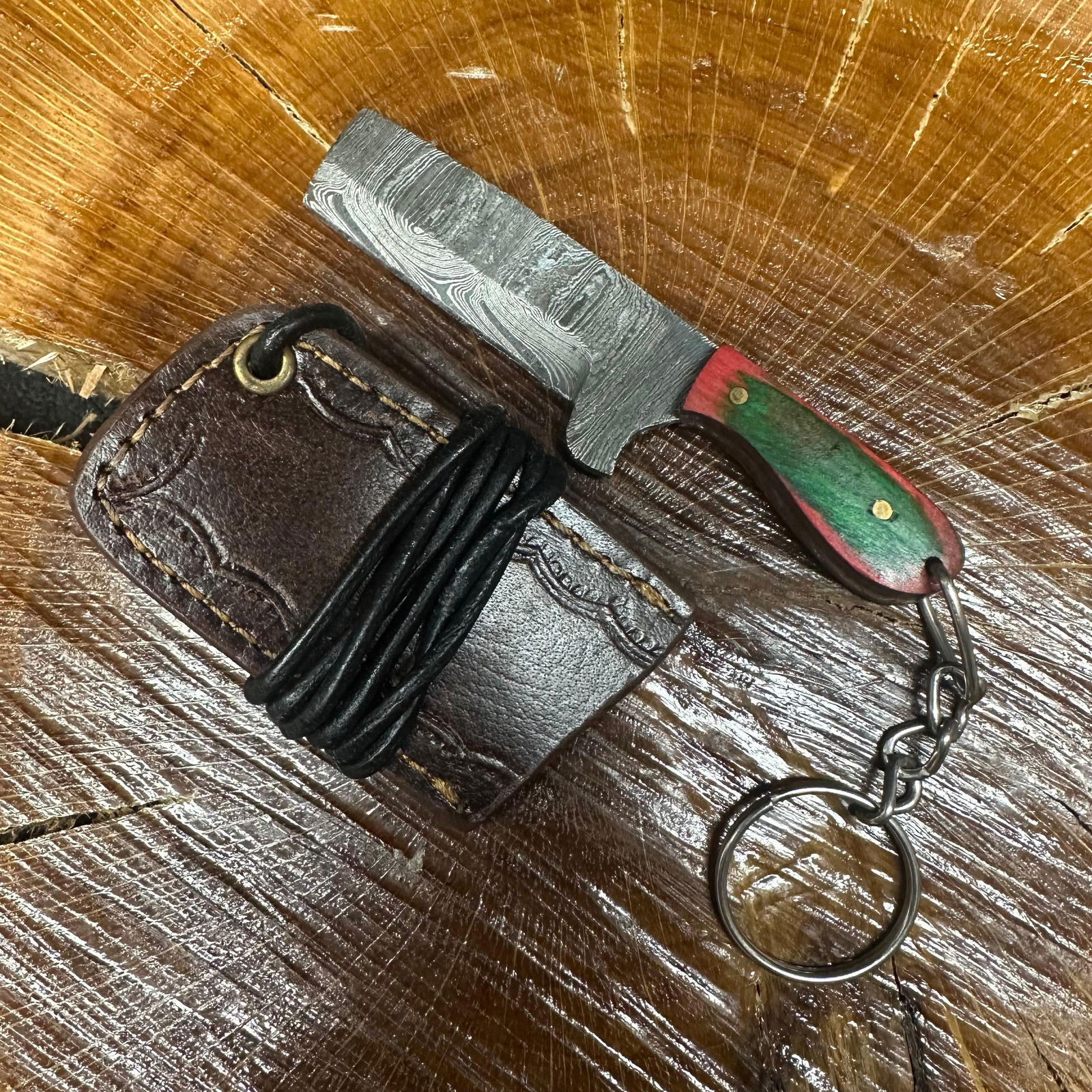 MHS Cutlery Keychain Cleaver Style Straight Blade Knife With Leather Case Necklace R43: Small key chain-sized fixed-blade knife featuring a patterned steel blade and a compact epoxy-resin/wood green/red-tone handle secured with brass pins. Includes a fitted brown leather sheath with